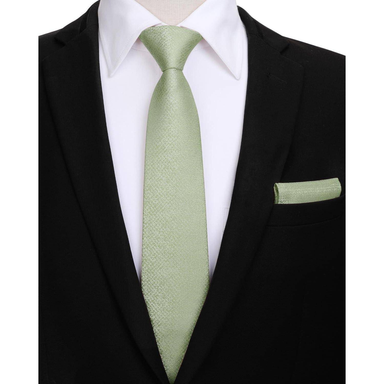 Eine Person, die einen schwarzen Anzug, ein weißes Hemd und eine hellgrüne Krawatte mit einem passenden Einstecktuch trägt, was eine formelle Garderobe andeutet.