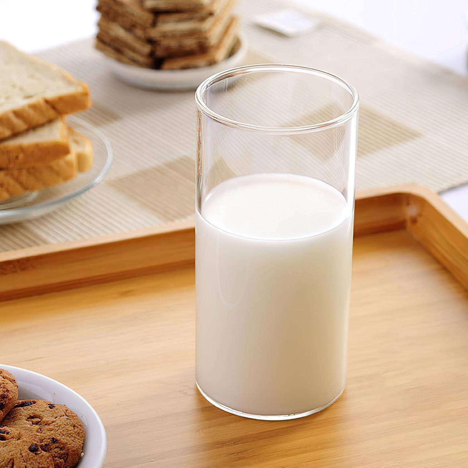 Ein Glas Milch steht auf einem Holztisch, umgeben von einem Teller mit Keksen und einem Stapel Brot.