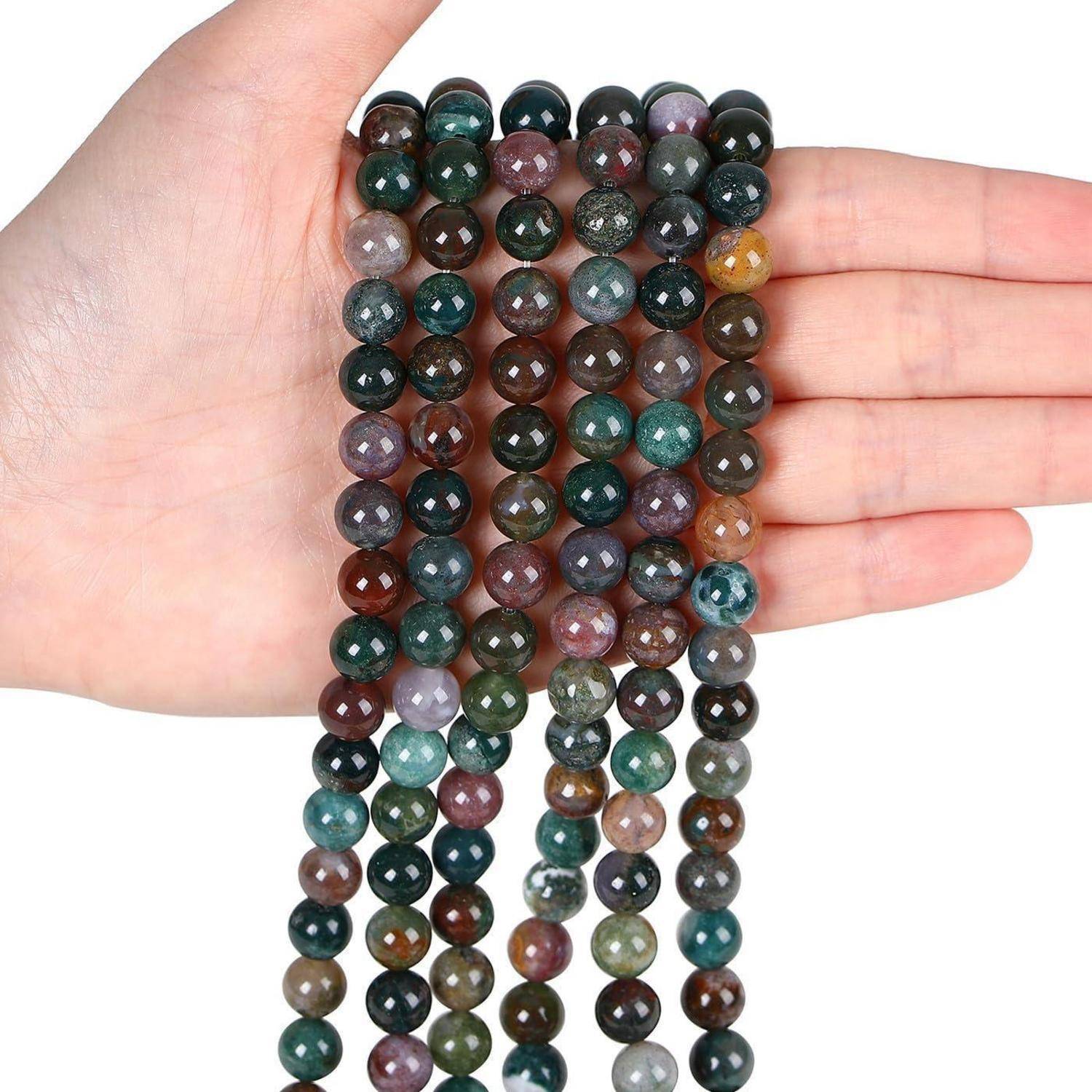 Eine Hand hält Stränge von polierten, mehrfarbigen Achatperlen, die Variationen von grünen, braunen, roten und violetten Farbtönen präsentieren.