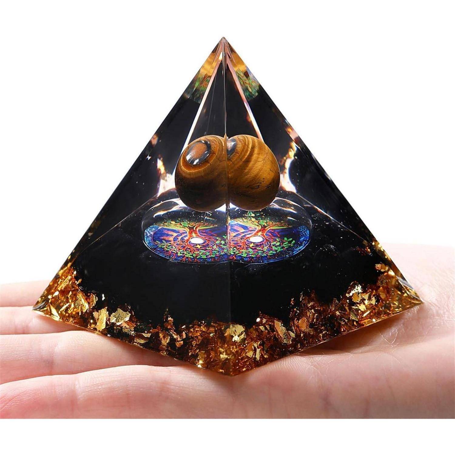 Eine Hand hält eine dekorative Pyramide mit einer Holzspirale im Inneren, die auf einer lebendigen, bunten Basis ruht. Goldflitter sind überall verstreut.