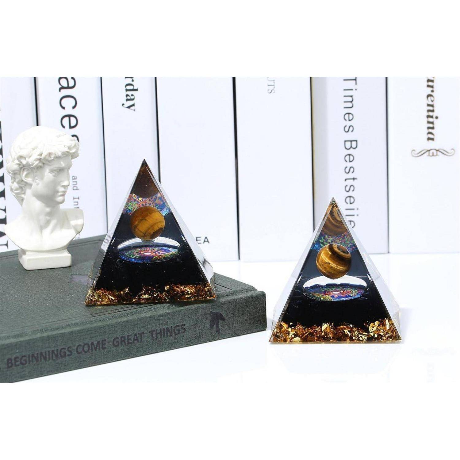 Zwei pyramidenförmige Objekte mit einem Galaxiendesign und einem Planeten darin sind auf einem Regal mit Büchern und einer kleinen Büste platziert.