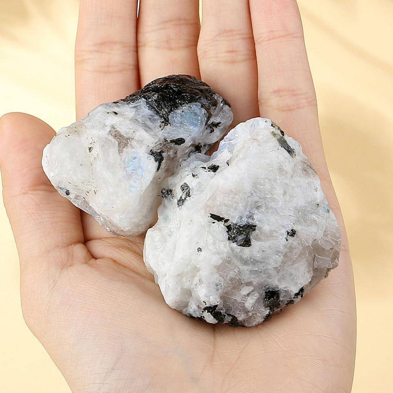 Eine Hand, die zwei große, weiße Steine mit schwarzen und grauen Sprenkeln hält, höchstwahrscheinlich Mineralproben, die vor einem neutralen Hintergrund präsentiert werden.