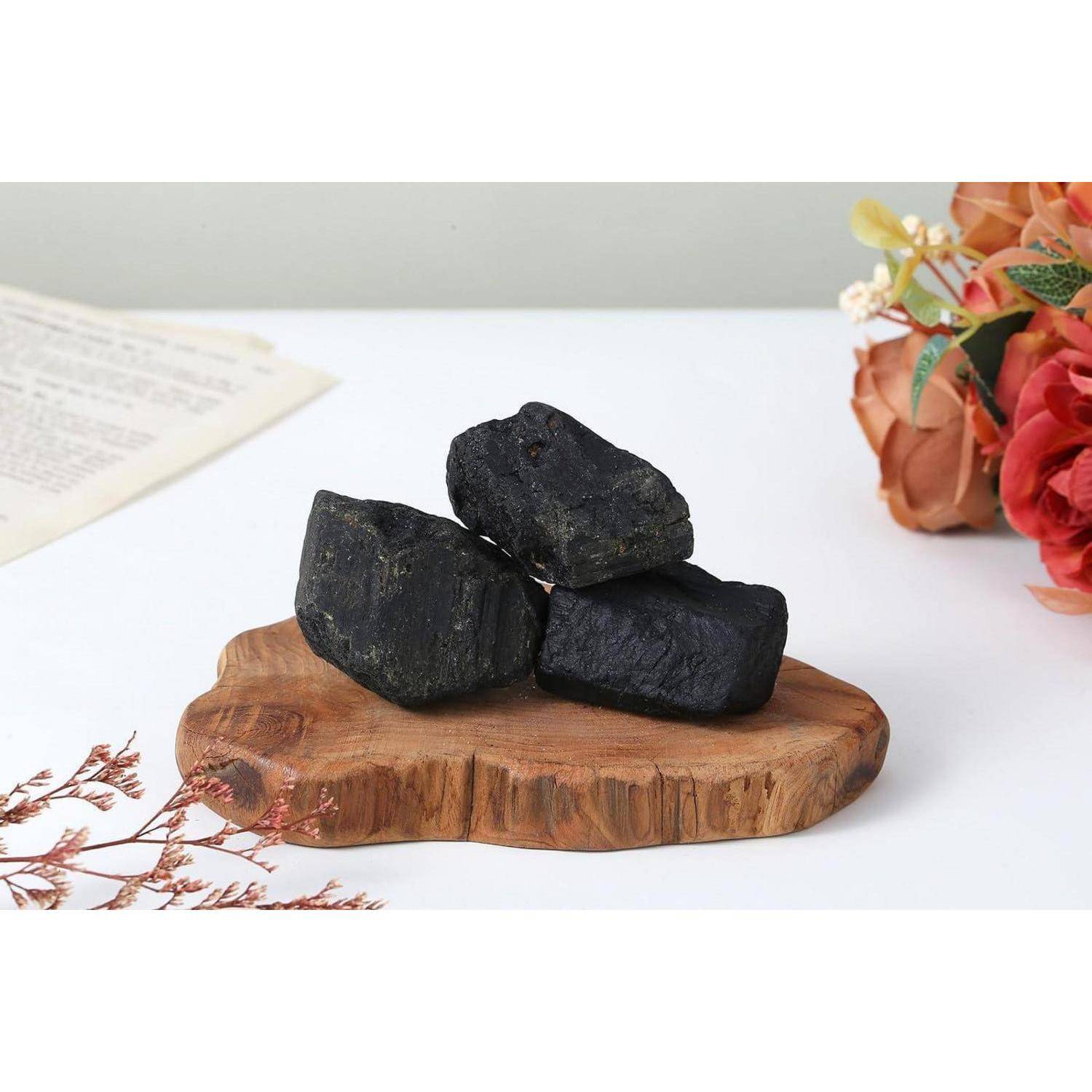 Drei schwarze Steine, angeordnet auf einem Holzbrett, platziert auf einer weißen Oberfläche mit orangen Blumen und einem Dokument im Hintergrund.