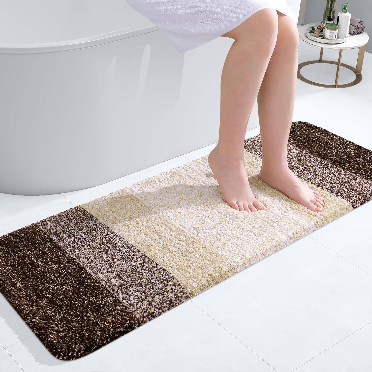 Frau mit überkreuzten Beinen sitzt auf der Badewanne, in ein weißes Handtuch gehüllt. Ein gestreifter braun-beiger Badematte liegt auf dem Badezimmerboden.