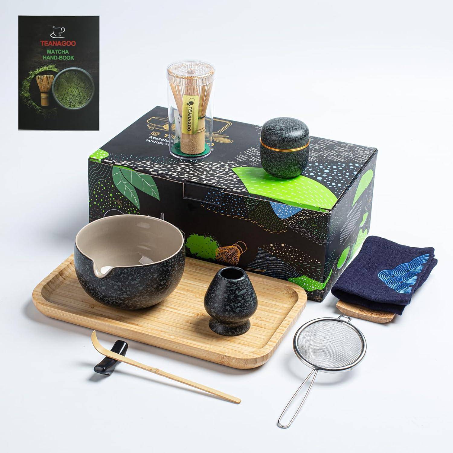 Eine Box mit Matcha-Tee-Set-Artikeln: Schale, kleiner Krug, Bambusbesen, Schöpflöffel, Bestenständer, Sieb und ein Tuch auf einem Holztablett.