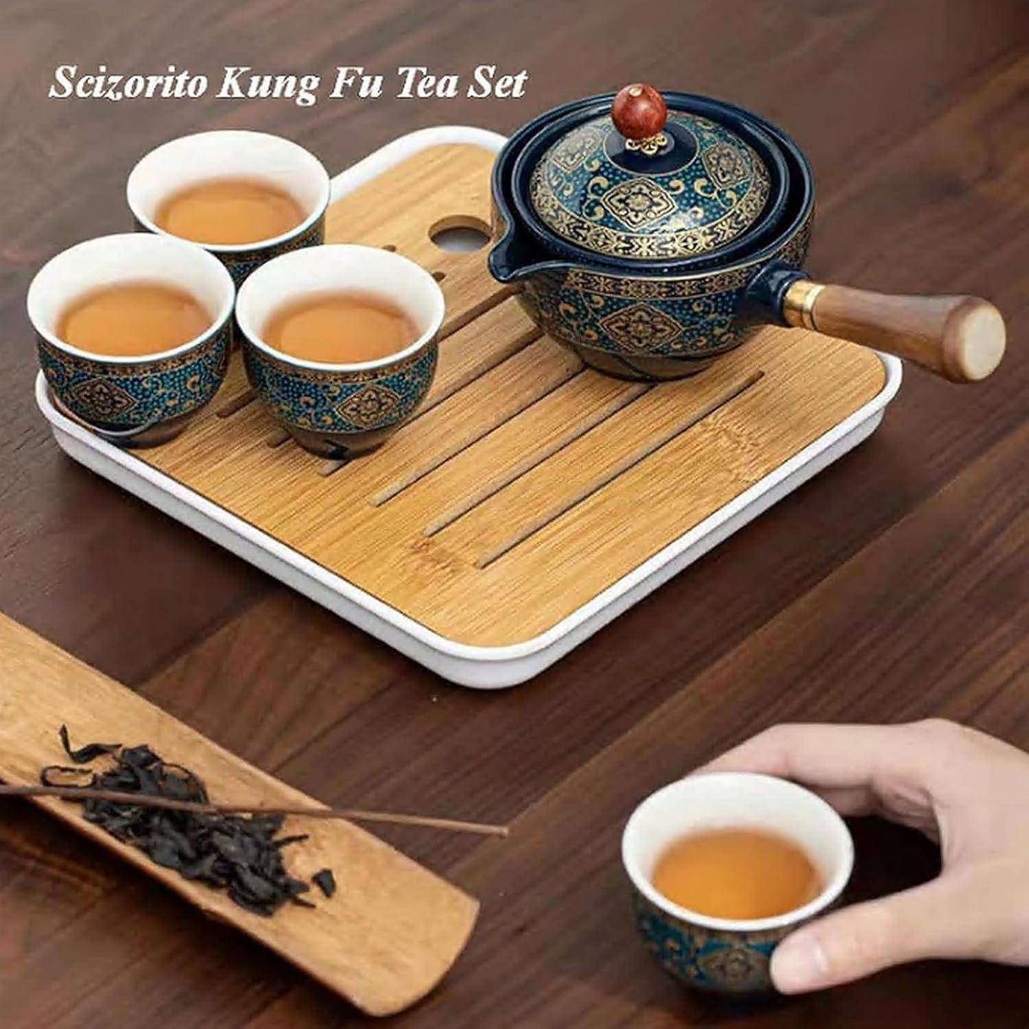 Ein Kung Fu Teeservice auf einem Holztablett, das drei verzierte Tassen und eine Teekanne mit einer Hand, die eine Tasse hält, sowie lose Teablätter in der Nähe umfasst.