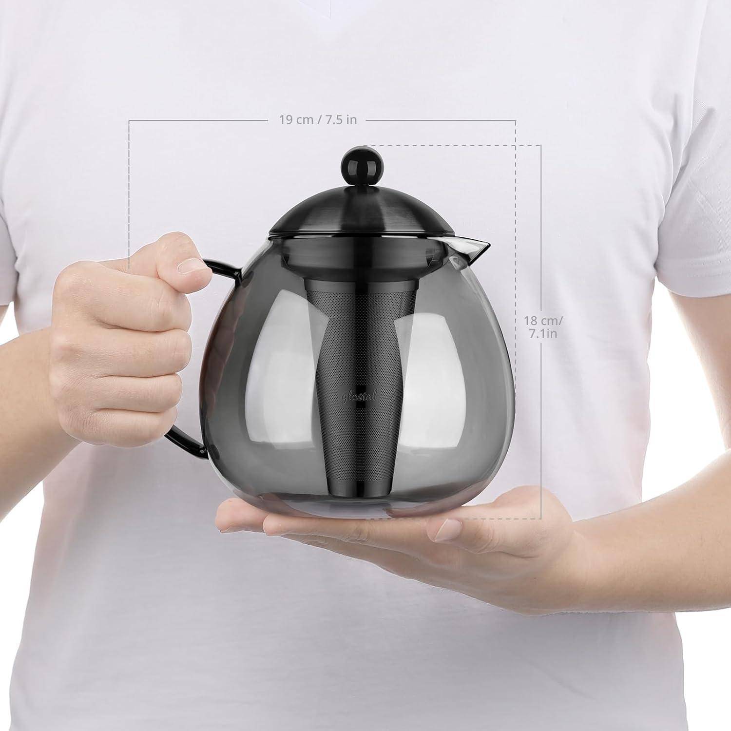 Eine Person hält eine transparente Teekanne mit einem schwarzen Deckel und Teesieb. Die Maße betragen: 19 cm (Breite), 18 cm (Höhe).