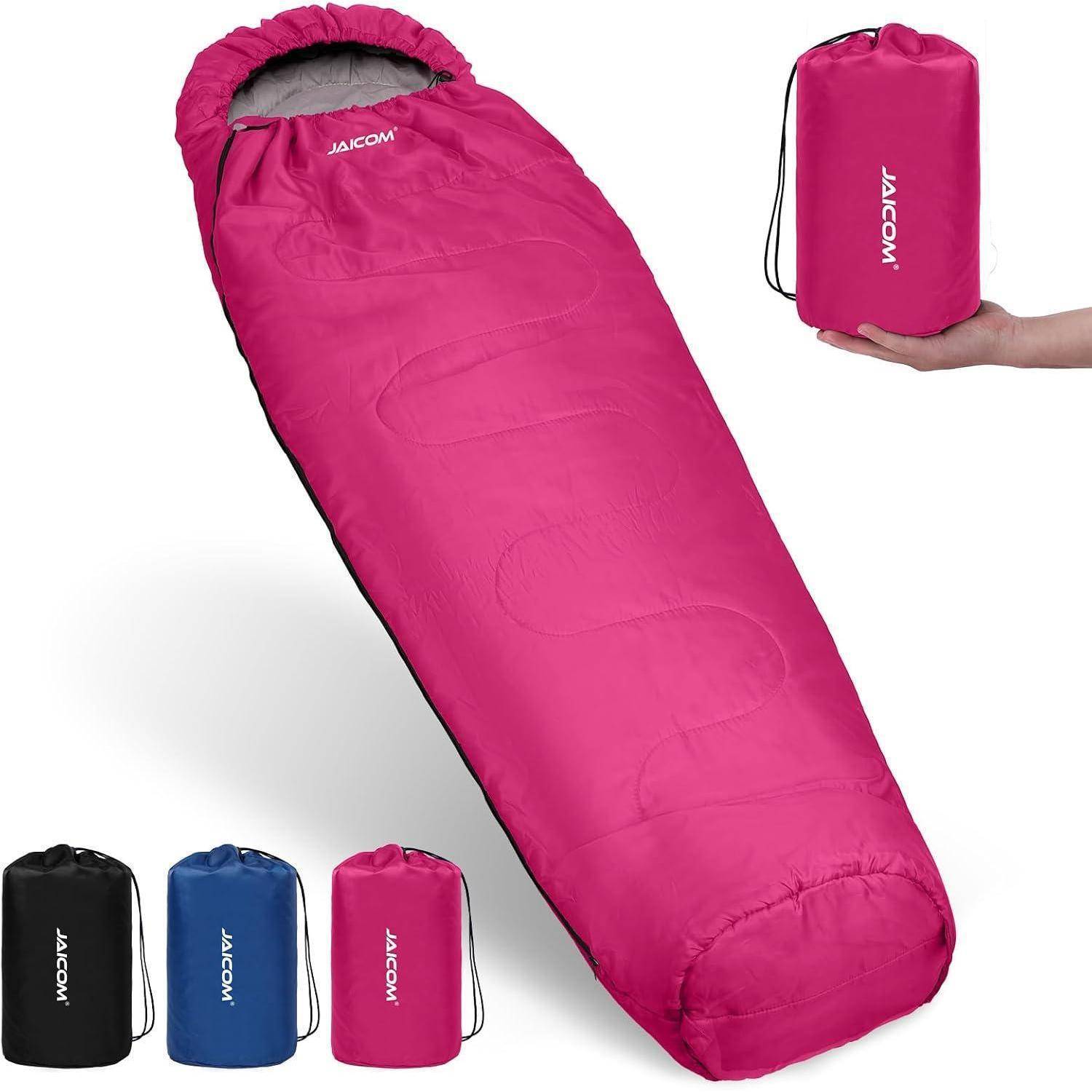 Ein rosa Schlafsack mit grauem Innenfutter wird gezeigt, zusammen mit seiner passenden Tragetasche in der Hand. Drei zusätzliche Tragetaschen in Schwarz, Blau und Rot befinden sich daneben.