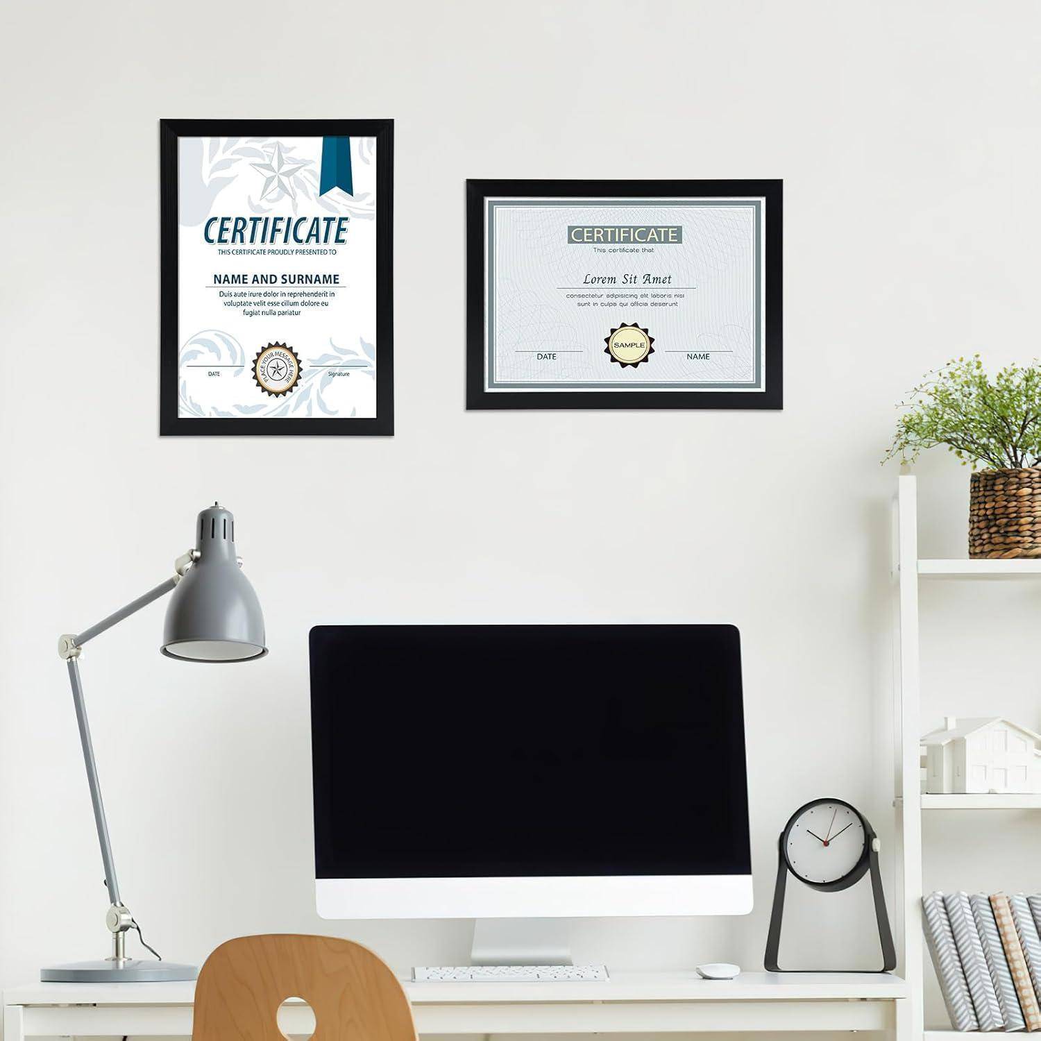 Zwei gerahmte Zertifikate an einer weißen Wand über einem Schreibtisch mit einer Lampe. Ein Regal mit Büchern und einer Pflanze befindet sich rechts.