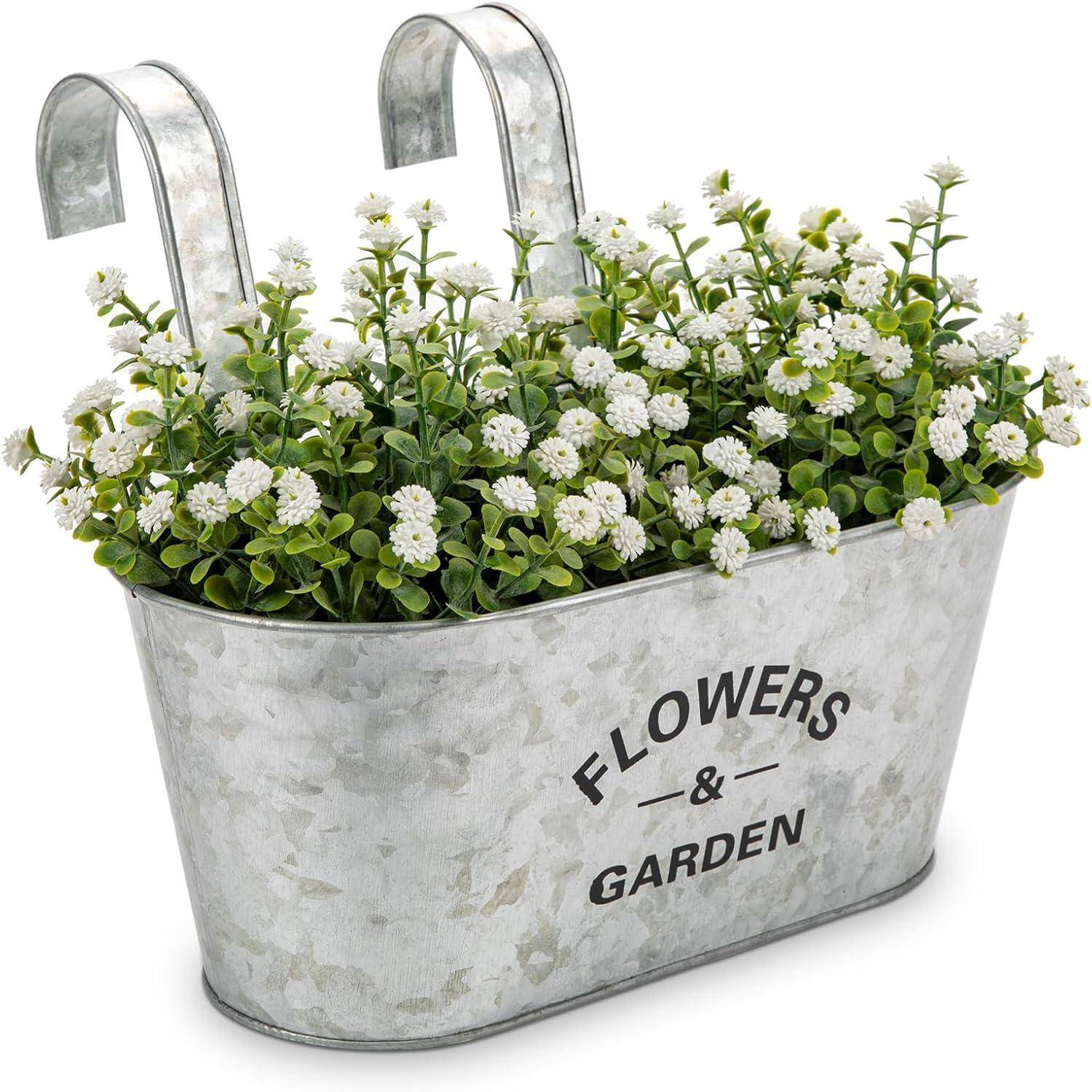 Metallpflanzer mit Haken, gefüllt mit weißen Blumen und grünem Blattwerk. Der Pflanzer ist mit 'BLUMEN & GARTEN' beschriftet.