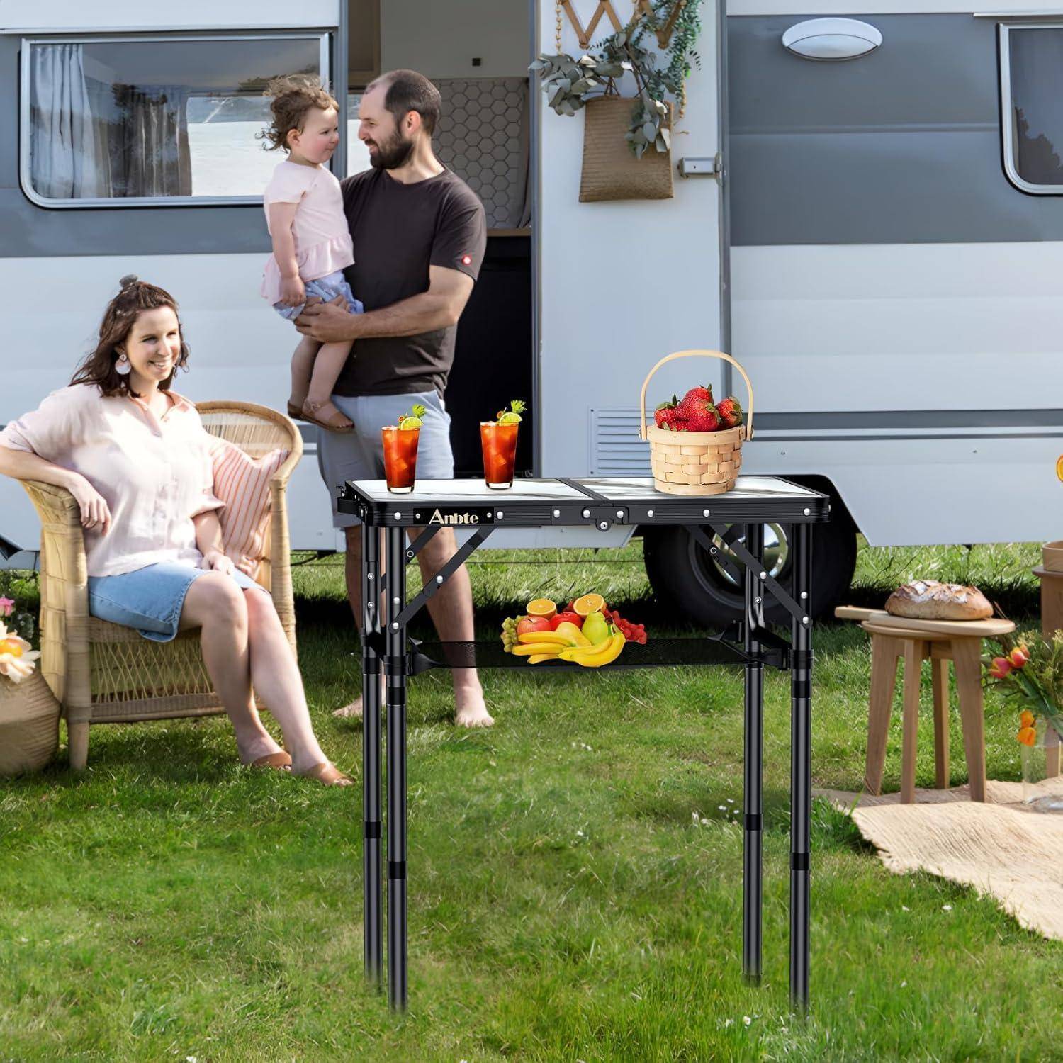 Eine Familie genießt einen sonnigen Tag vor einem Wohnwagen. Eine Frau sitzt lächelnd, ein Mann hält ein Kind, und im Vordergrund steht ein Tisch mit Getränken und einem Korb.