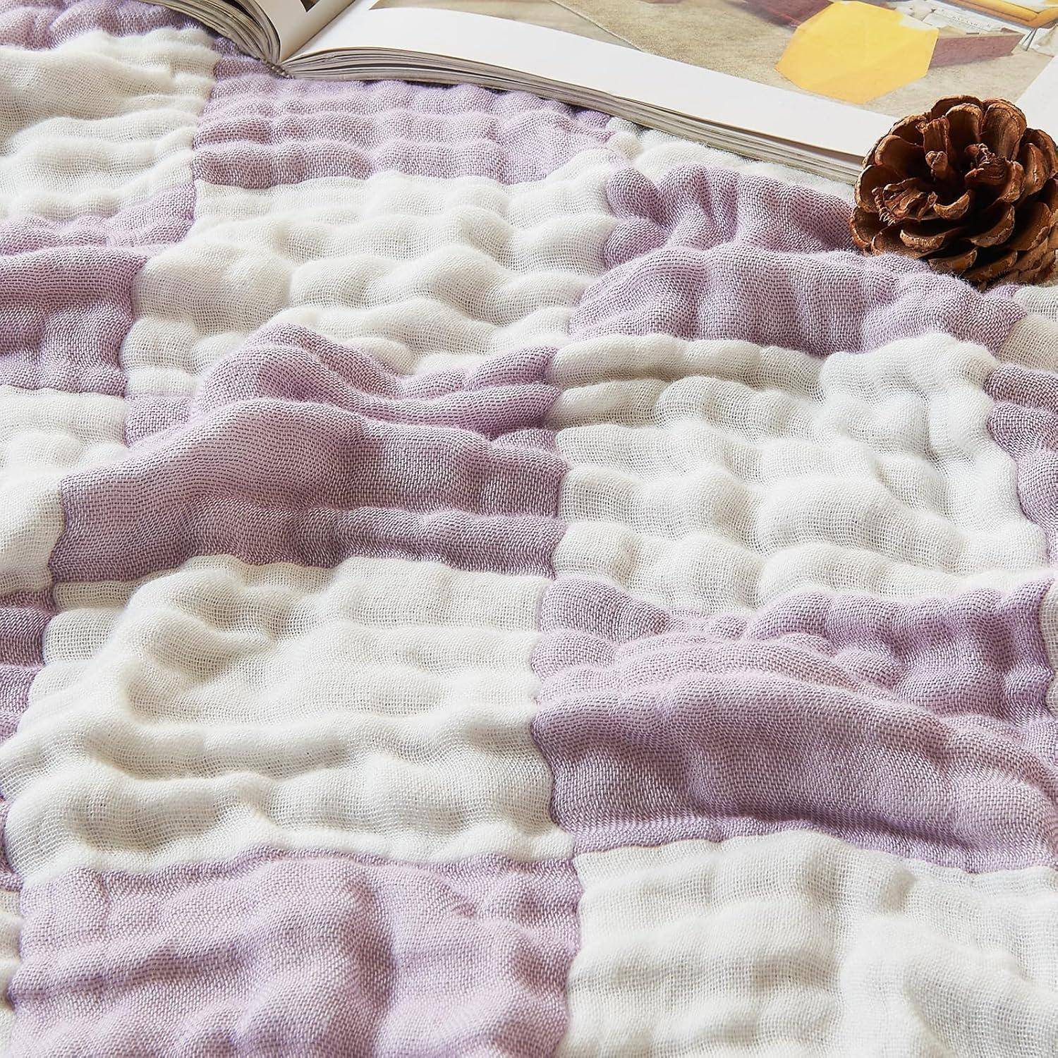 Eine weiche, strukturierte Decke mit Lavendel- und weißen Streifen ist ausgebreitet, mit einer Tannenzapfen darauf, die neben einem offenen Buch liegt.