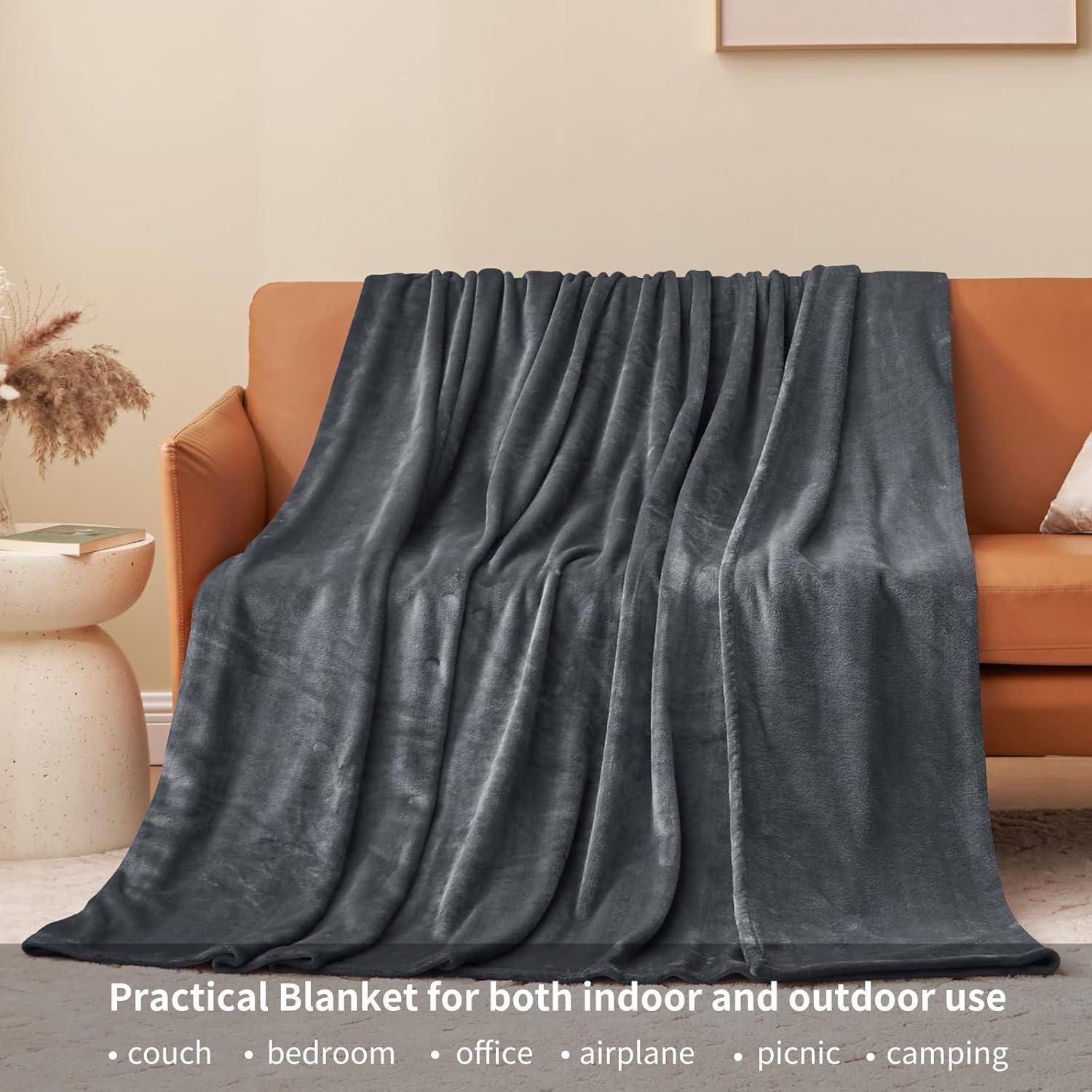 Eine dunkelgraue Decke, die über einem beigen Sofa in einem Raum mit minimalistischer Einrichtung drapiert liegt und ihre vielseitige Nutzung für Innen- und Außenbereiche betont.