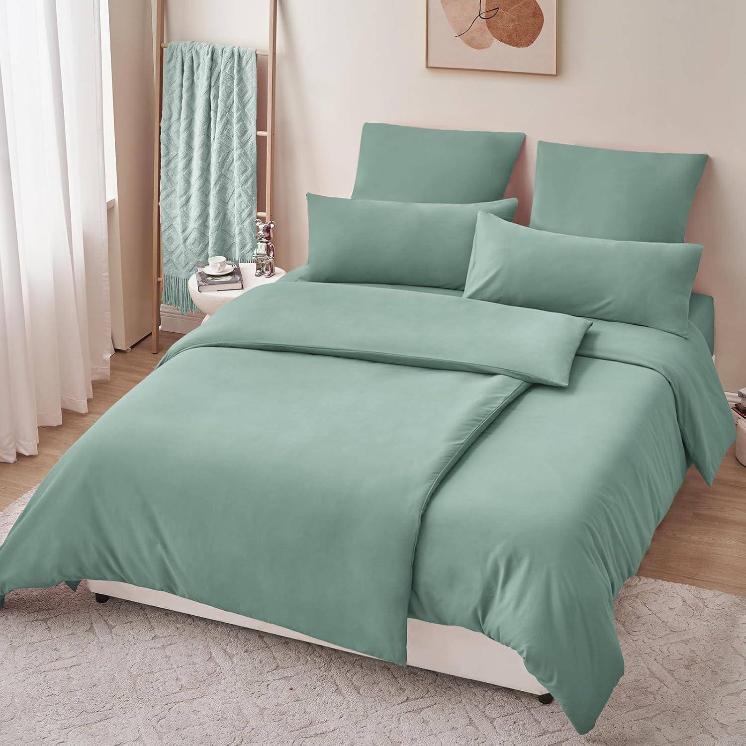 Ein sauber gemachtes Bett mit petrolblauer Bettwäsche, zwei großen Kissen, zwei kleinen Dekokissen und einer passenden Decke. Ein Handtuch hängt an einem Ständer neben dem Bett.