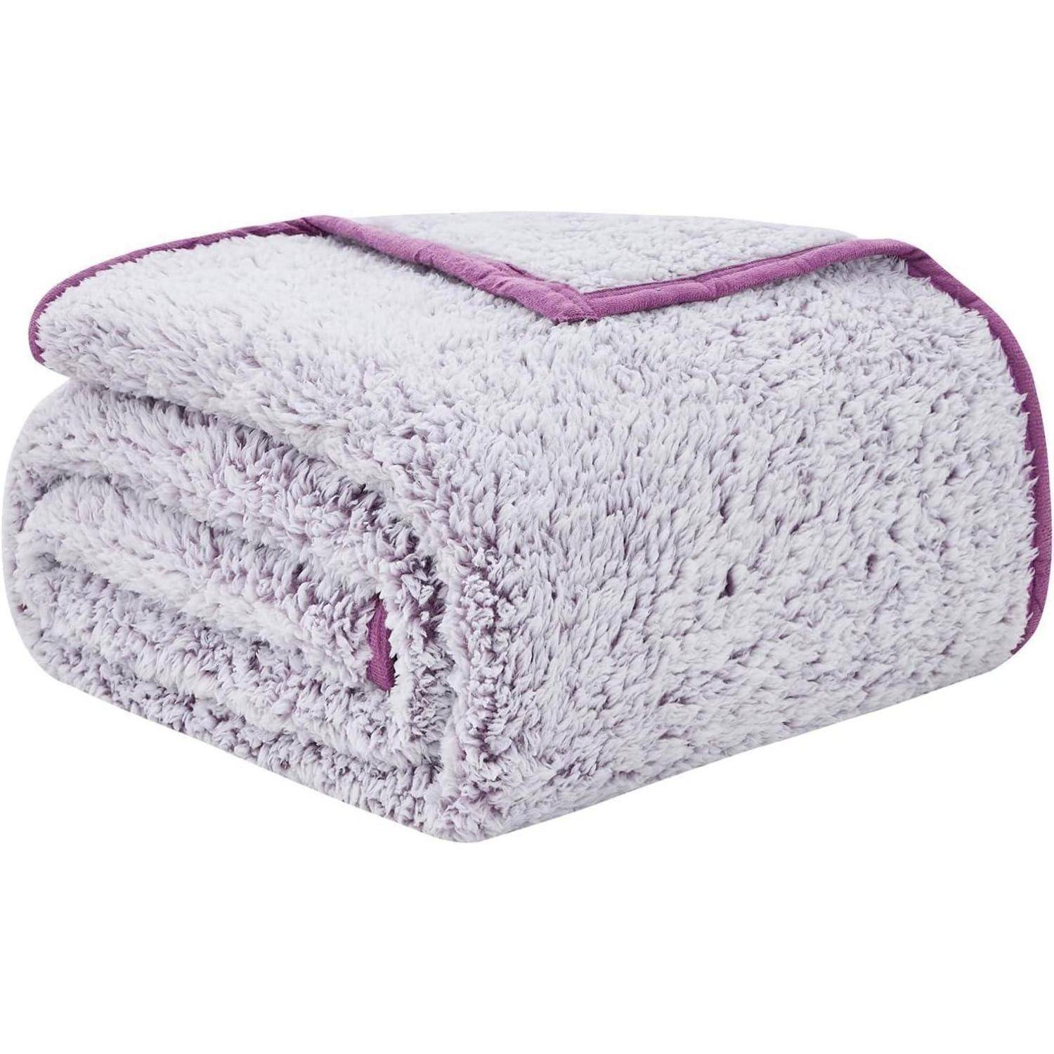 Eine gefaltete, flauschige hellgraue Decke mit violetten Einfassungen wird gezeigt, die ihre Weichheit und Wärme betont.