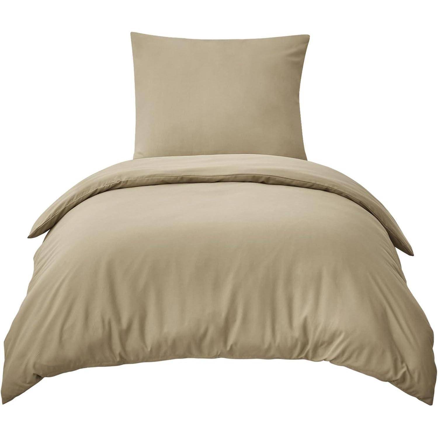 Ein beiges Bettdecken-Set auf einem bezogenen Bett, bestehend aus passendem Kissen und Steppdecke.
