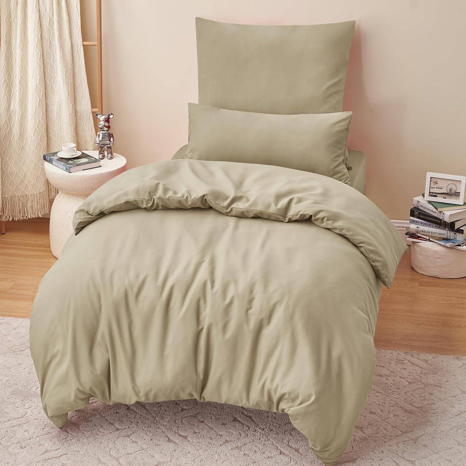 Ein beige gehaltenes, ordentlich gemachtes Bett mit passenden Kissen und Bettdecke, neben einem runden Tisch mit Büchern, einer Tasse und einer Kerze, in einem gemütlichen Schlafzimmer.