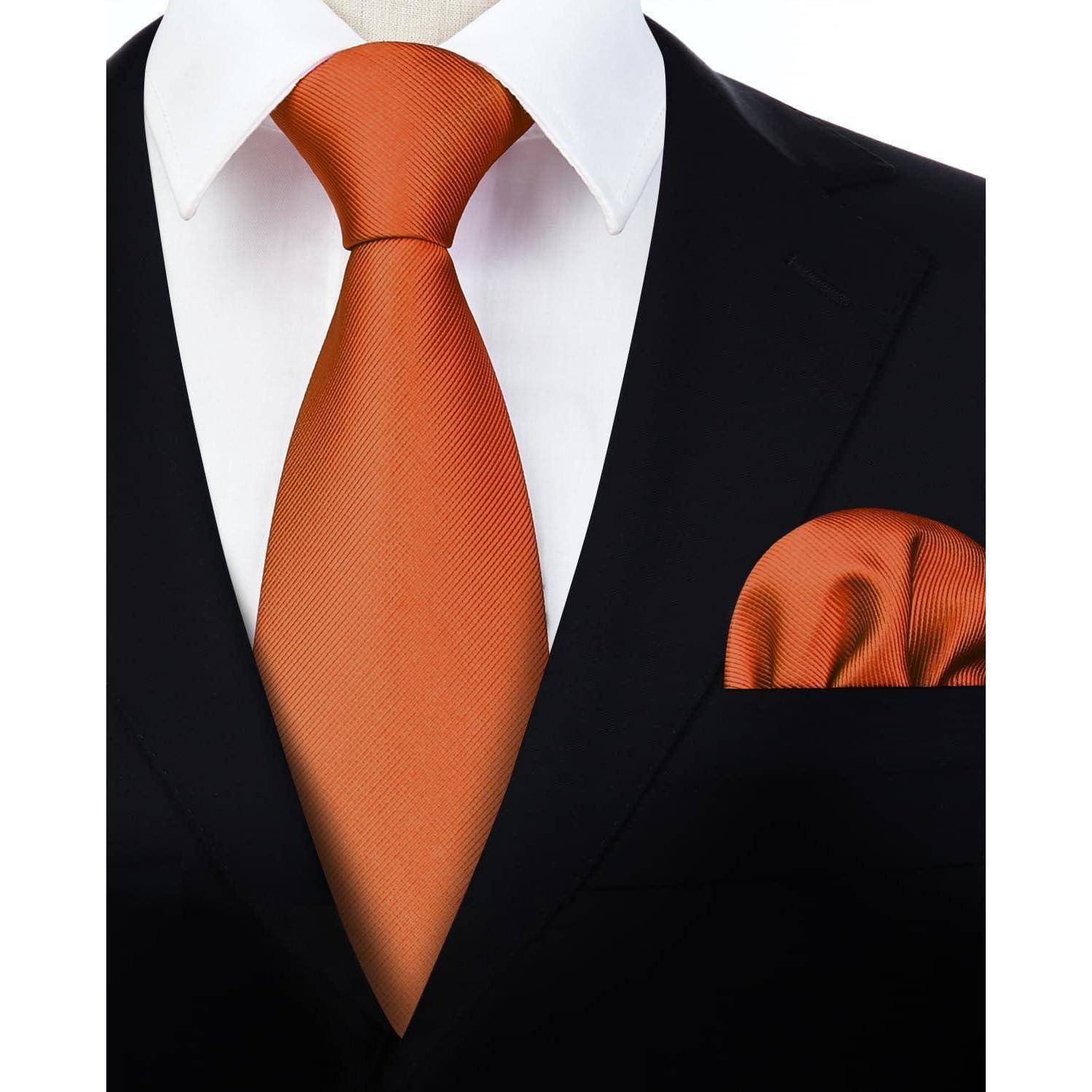 Eine Person in einem schwarzen Anzug mit weißem Hemd, orangefarbener Krawatte und passendem orangefarbenen Einstecktuch.
