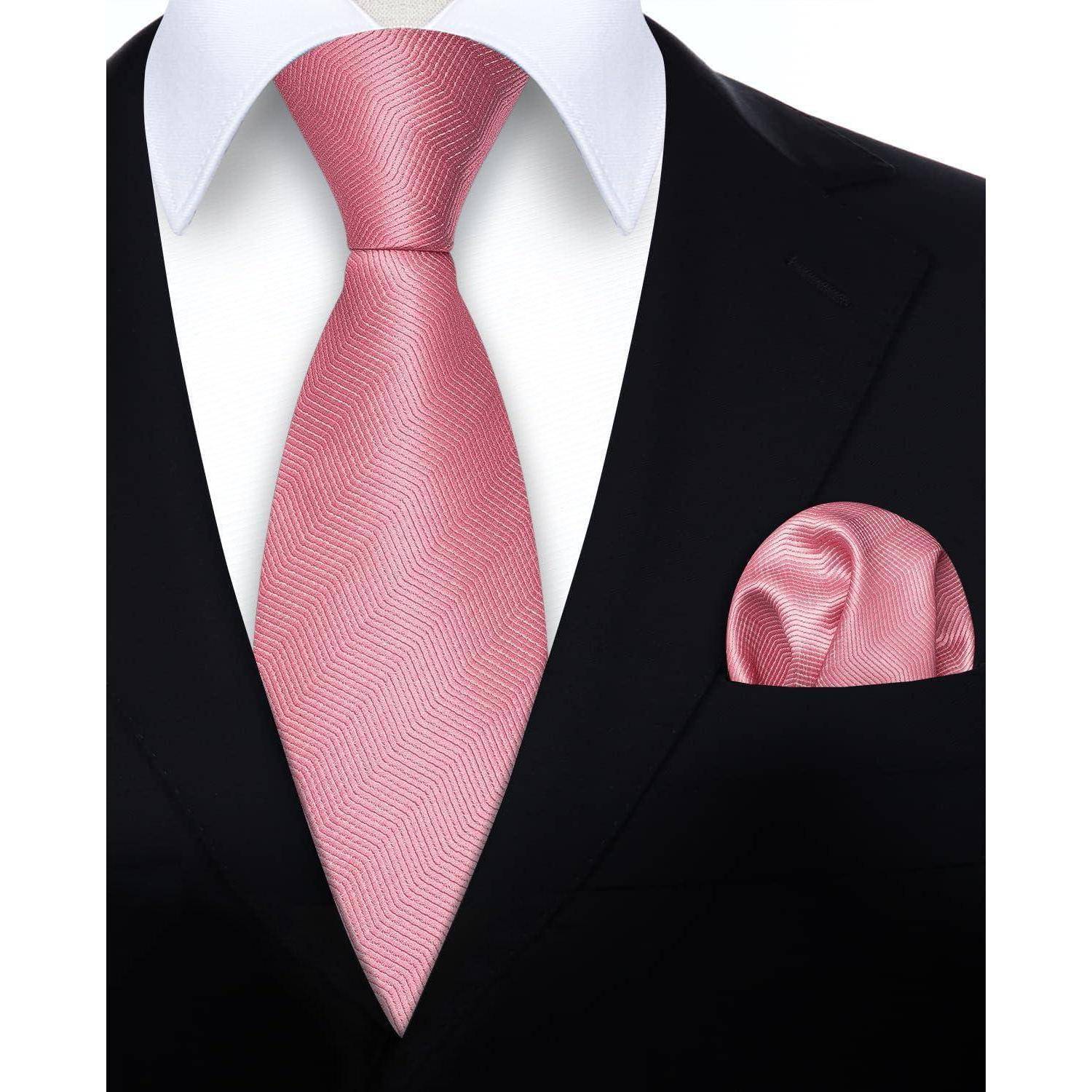 Eine Nahaufnahme einer Person, die einen schwarzen Anzug mit einem weißen Hemd, einer pinken Krawatte und einem passenden pinken Einstecktuch trägt.