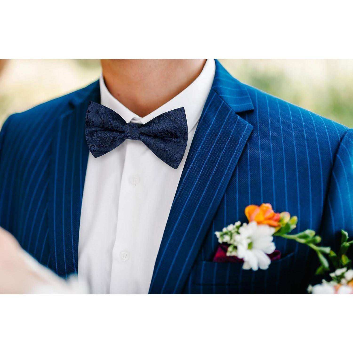 Eine Person trägt einen blauen Nadelstreifenanzug mit einer dunkelblauen Fliege und weißem Hemd. Eine farbenprächtige Ansteckblume ist an der Reverskante angesteckt.