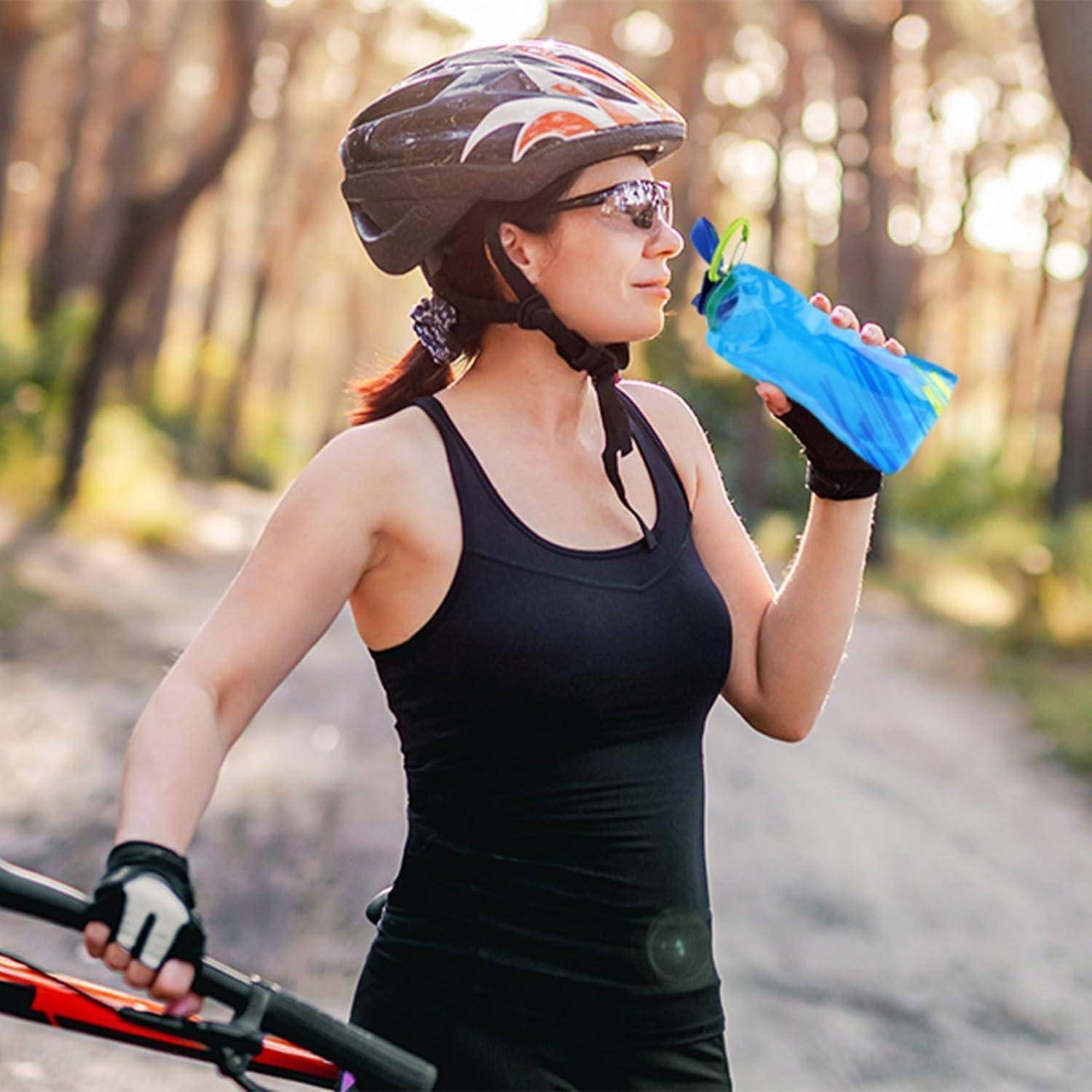 Eine Frau mit Helm und Sonnenbrille steht auf einem sonnenbeschienenen Waldweg und hält eine blaue Wasserflasche und ein Fahrrad.