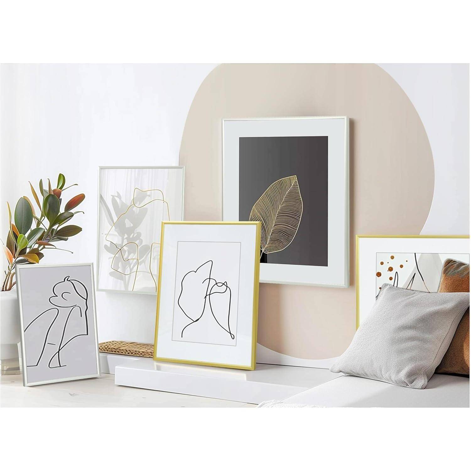 Eine Vielzahl von gerahmten abstrakten und botanischen Kunstwerken sind vor einem pastellfarbenen Hintergrund ausgestellt, darunter Linienzeichnungen und Blattdrucke.