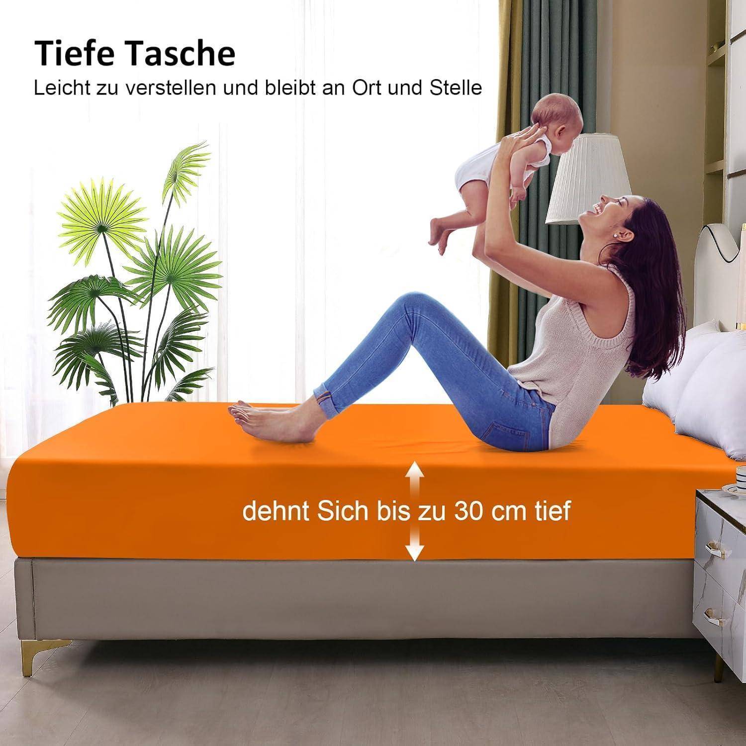 Eine Frau auf einem orangefarbenen Bett hält ein Baby in die Höhe. Der deutsche Text erwähnt ‚Deep Pocket', was auf eine Verstellbarkeit und Tiefe von bis zu 30 cm hinweist.