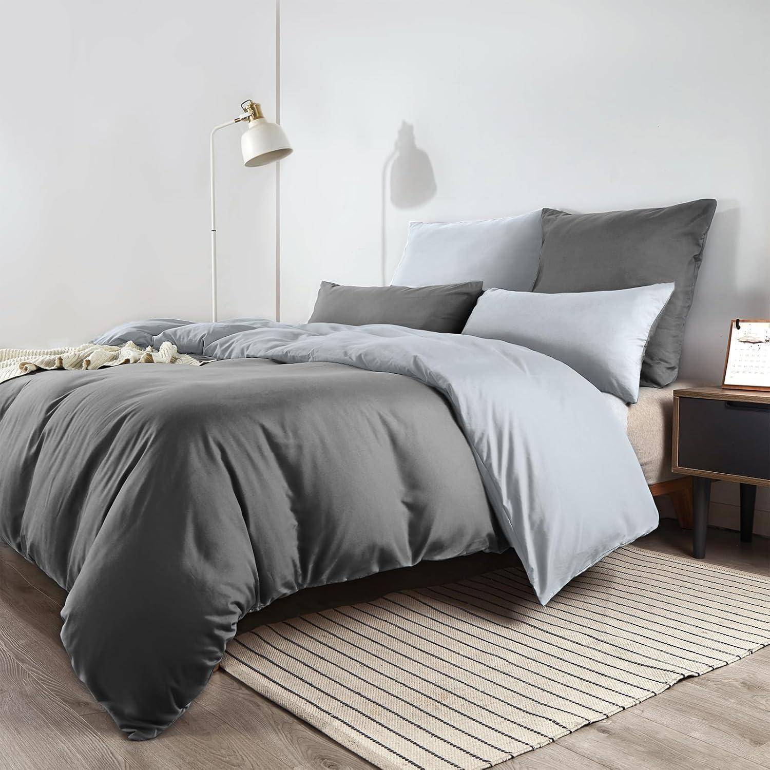 Ein ordentlich gemachtes Bett mit grau-blauer Bettwäsche in einem modernen Schlafzimmer, ausgestattet mit einer Stehlampe und einem Nachttisch.