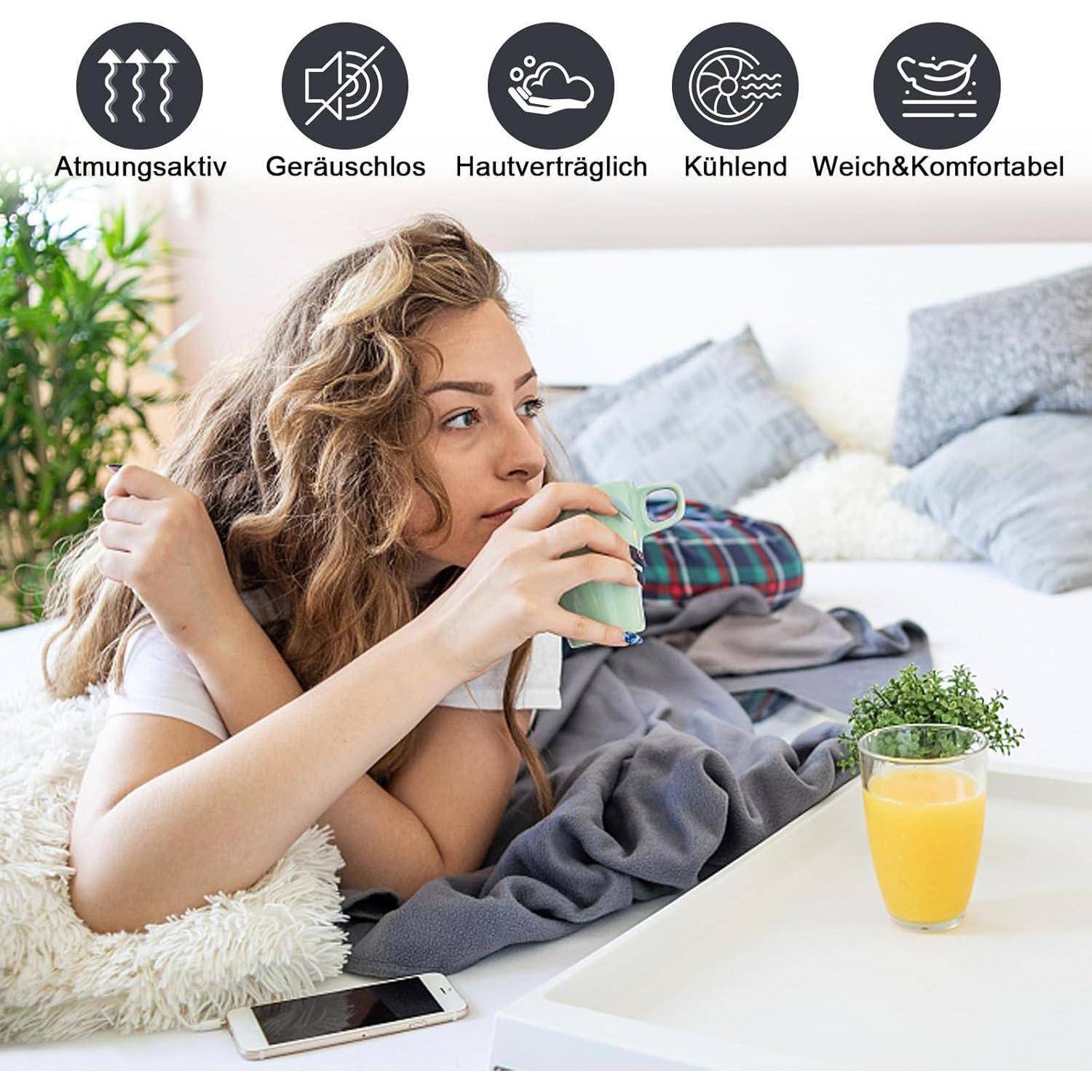 Eine Frau entspannt sich im Bett mit einem Drink, umgeben von Kissen. Symbole darüber heben Eigenschaften hervor: atmungsaktiv, leise, hautfreundlich, kühlend, bequem.