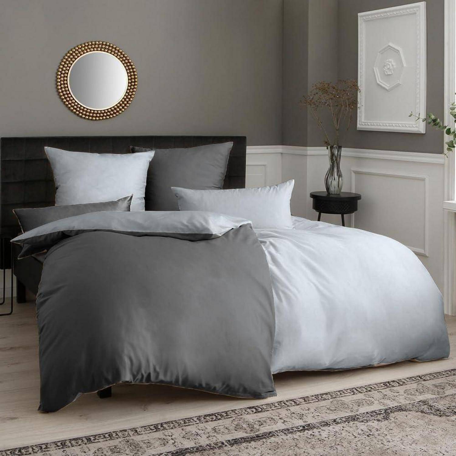 Ein ordentlich gemachtes Bett mit grauen und weißen Bettwäsche, Kissen und einem dekorativen Wandspiegel in einem modernen Schlafzimmerambiente.