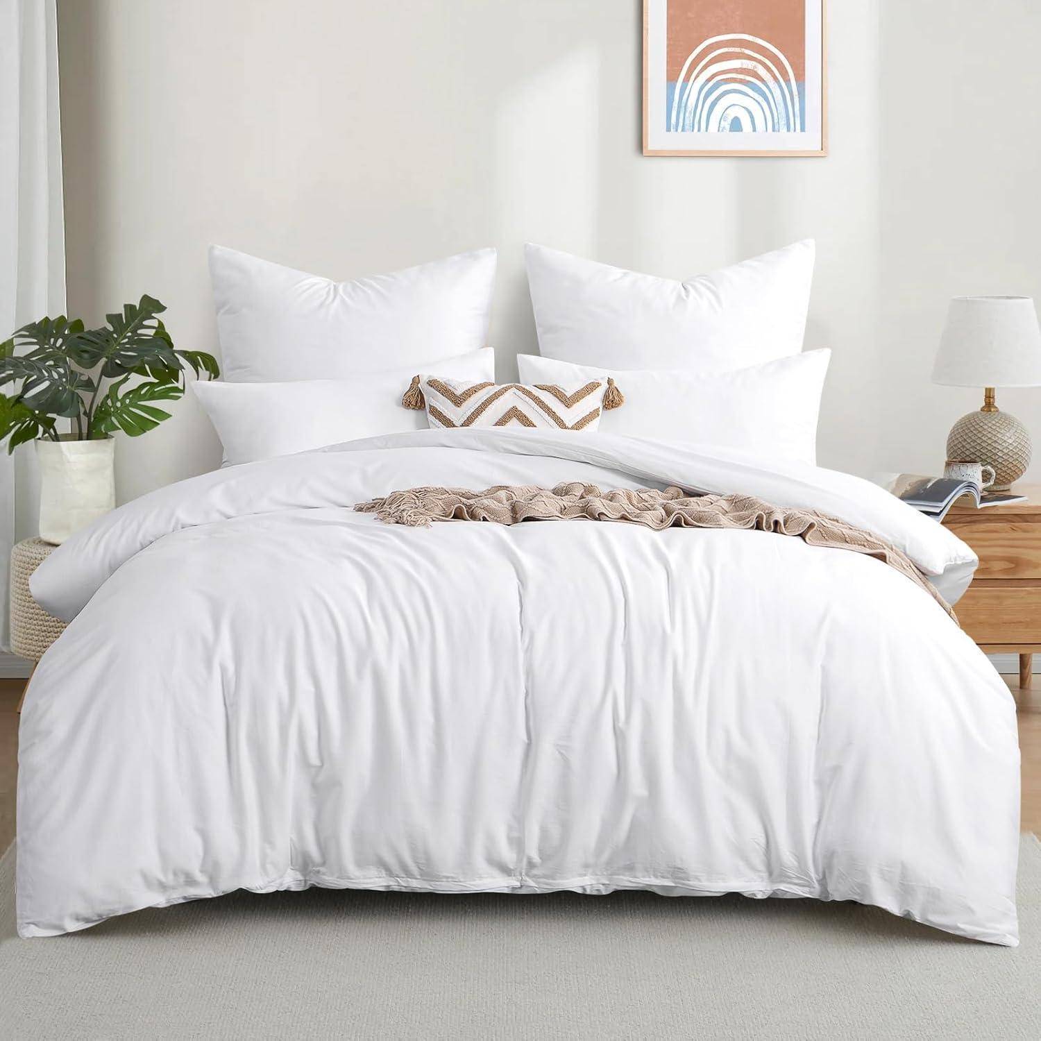 Ein ordentlich gemachtes Bett mit weißer Bettwäsche, zwei Kissen und einem beigen Überwurf. In der Nähe befinden sich eine Pflanze und ein Holznachttisch mit einer Lampe.