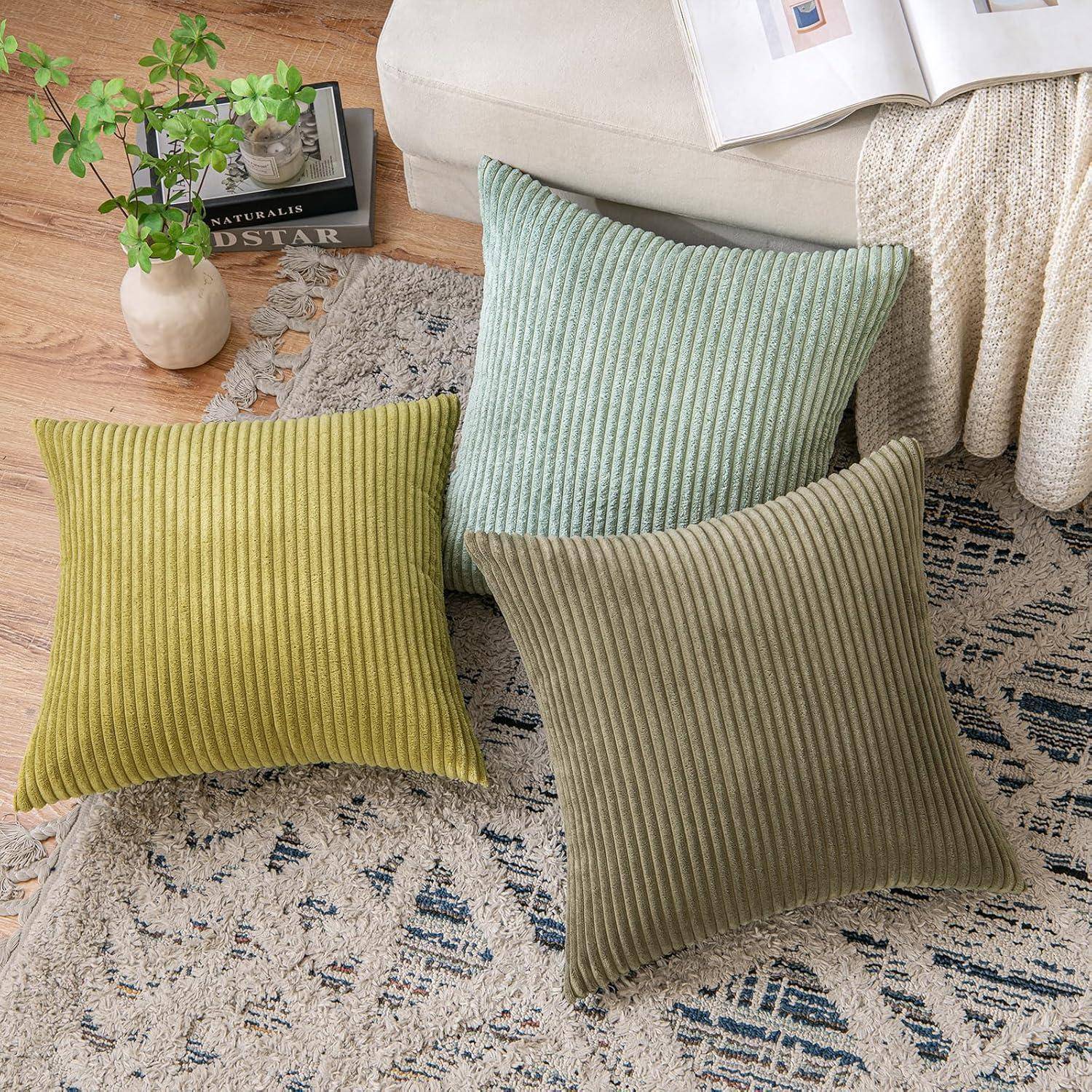 Kissen in Grün- und Beigetönen sind auf einem gemusterten Teppich platziert, mit einer weichen Decke und einem Buch auf einem hellgefärbten Sofa in der Nähe.