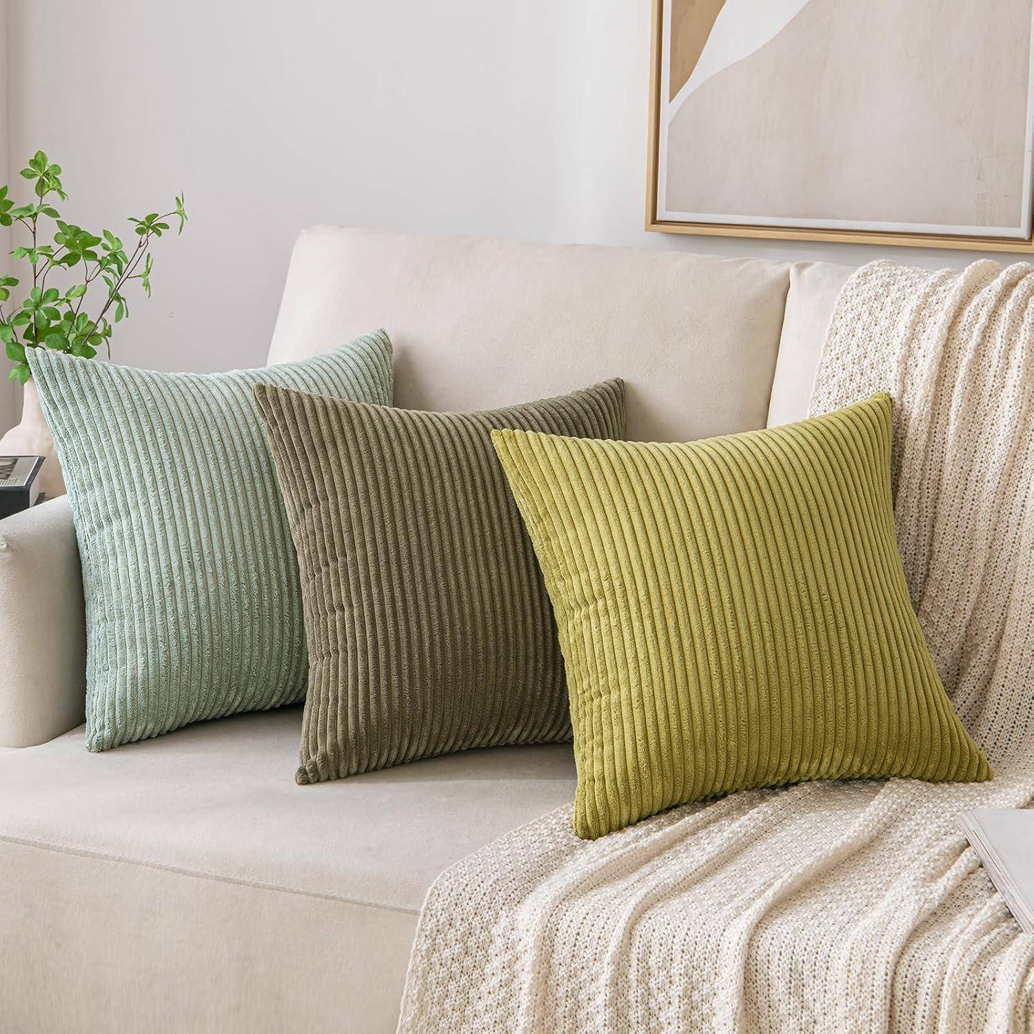 Ein beige Sofa mit grünen, grauen und senffarben gerippten Kissen, einer strukturierten Decke, die über die Seite gehängt ist, und einem gerahmten abstrakten Bild darüber.