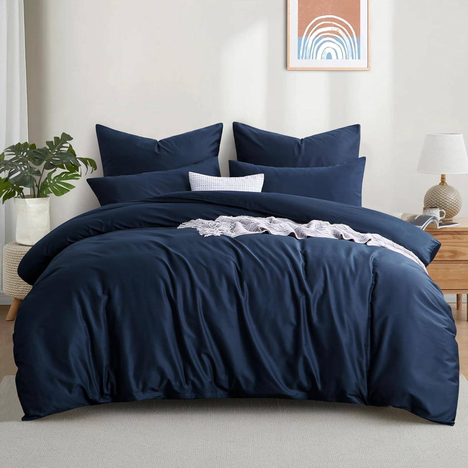 Ein sorgfältig gemachtes Bett mit dunkelblauen Bettwäscheüberzügen, ergänzt durch dekorative Kissen. Ein kleiner Pflanze und eine Lampe stehen auf dem Nachttisch und tragen zur gemütlichen Atmosphäre des Zimmers bei.
