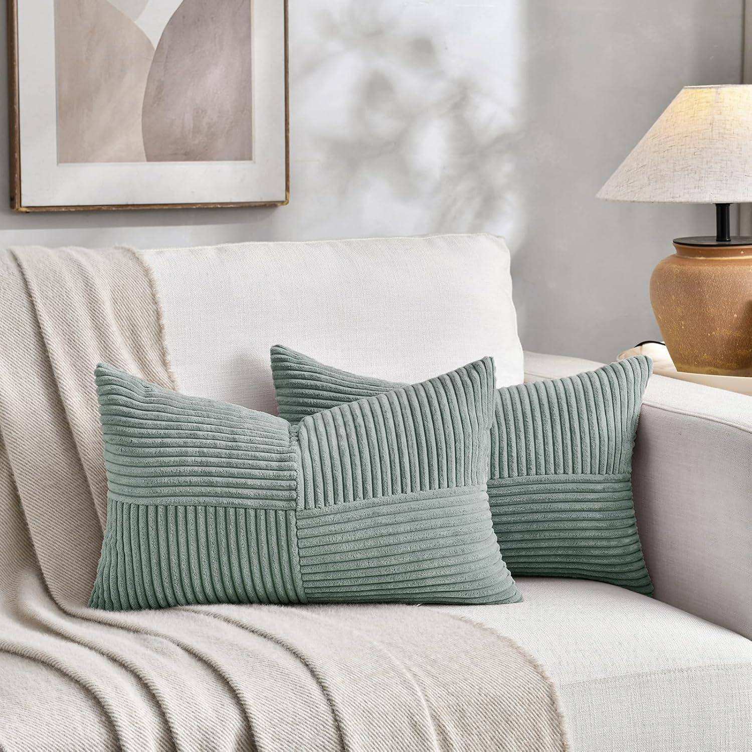 Kissen mit strukturiertem Muster ruhen auf einem hellen Sofa, unter einem gerahmten abstrakten Kunstwerk und einer beleuchteten Lampe, wodurch eine gemütliche Atmosphäre entsteht.
