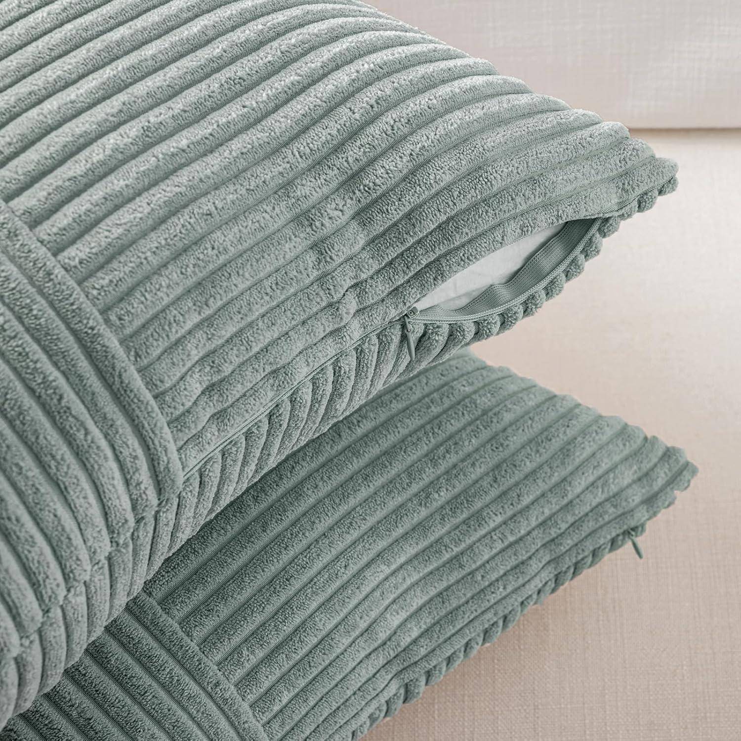 Zwei gestapelte, strukturierte petrolfarbene Kissen auf einem beigen Sofa, die mit ihrem gerippten Design einen Hauch von modernem Stil in die Einrichtung bringen.