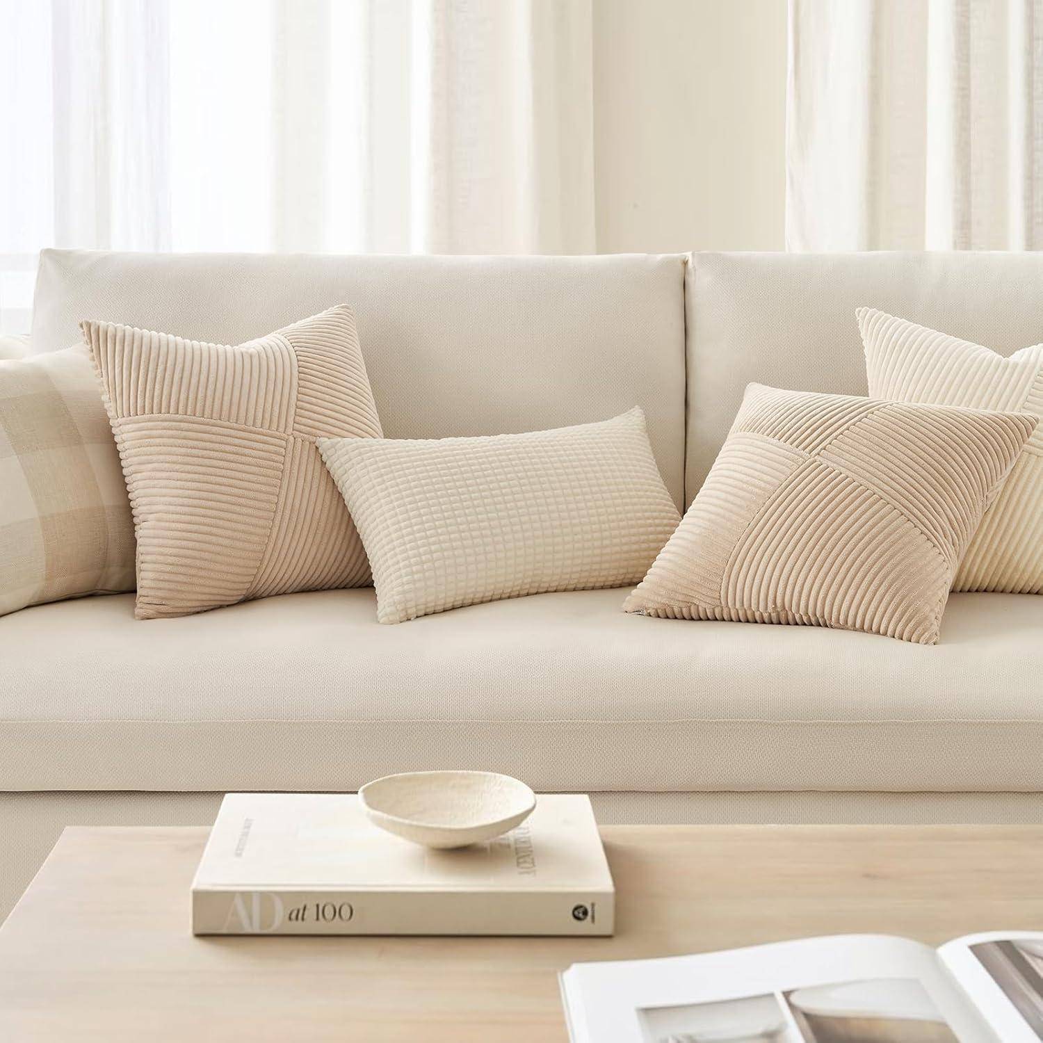 Ein beiger Sofa mit strukturierten, beigen Kissen und einem karierten Kissen. Ein minimalistischer, hellbrauner Couchtisch trägt ein Buch und eine kleine Schale.