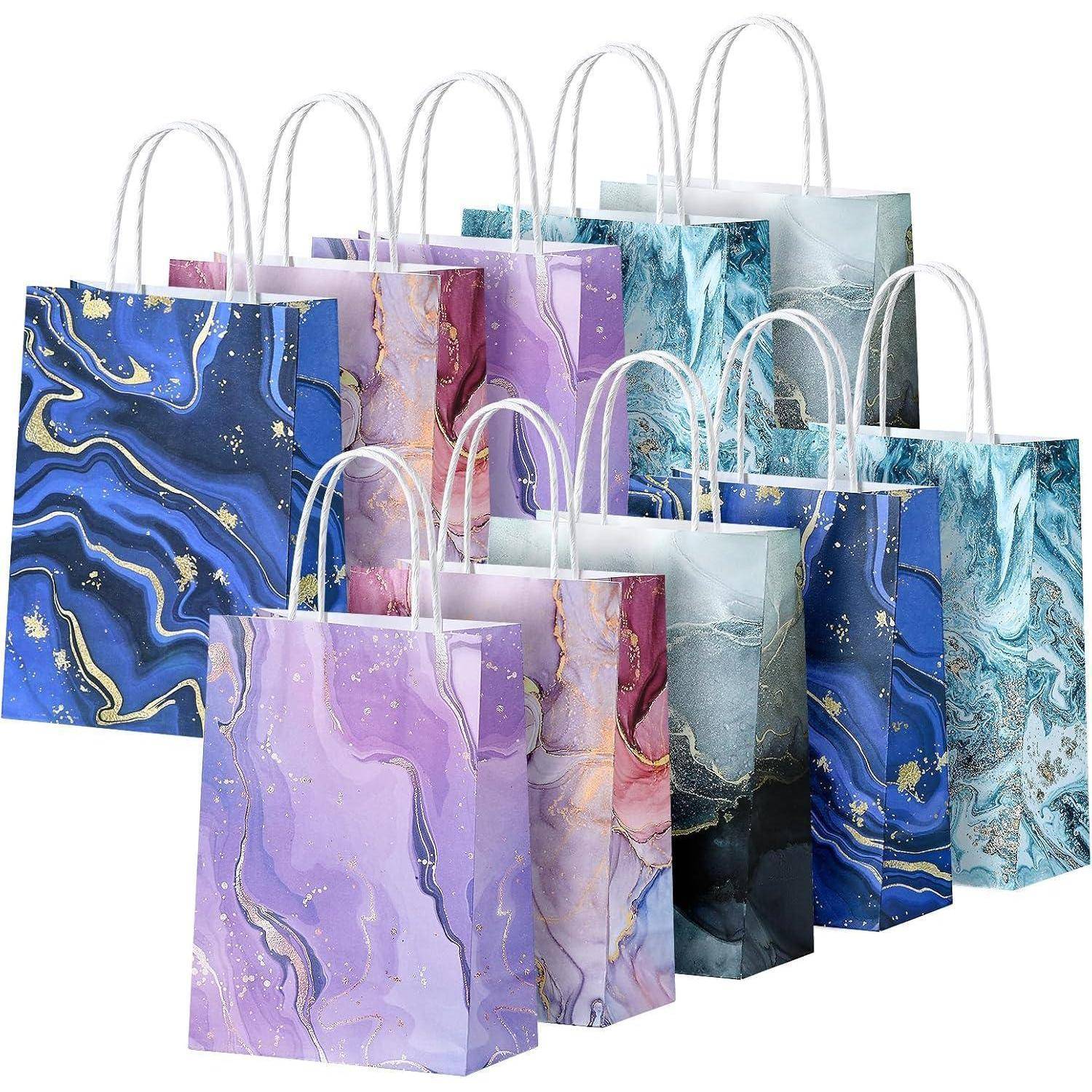 Mehrere Geschenktüten mit abstrakten Marmormustern in Blau-, Violett- und Rosatönen, mit weißen Henkeln.