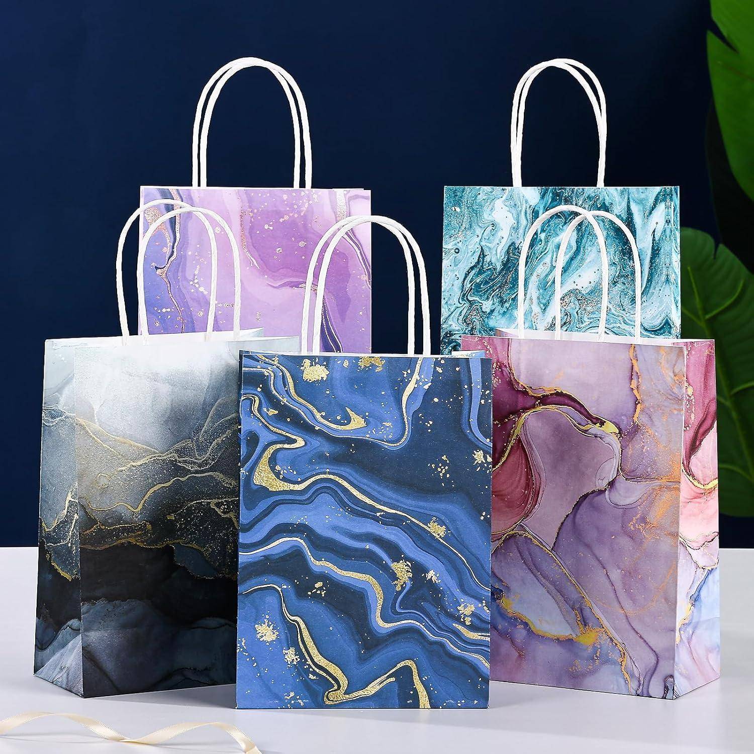 Bunte Geschenktüten mit Marmormustern in Blau-, Lila- und Rosatönen, die vor einem dunklen Hintergrund angeordnet sind und ihre Designs hervorheben.