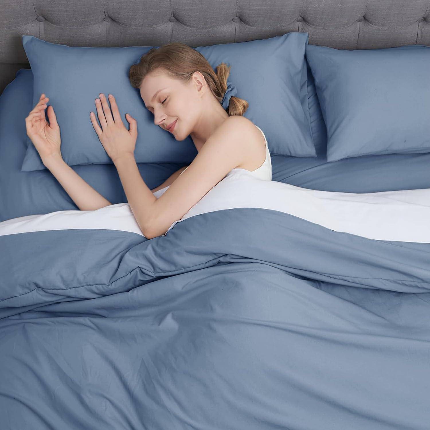 Eine Frau schläft friedlich auf einem Bett mit blauen Laken und Kissen, lächelt selig und wird von sanftem Licht umhüllt.