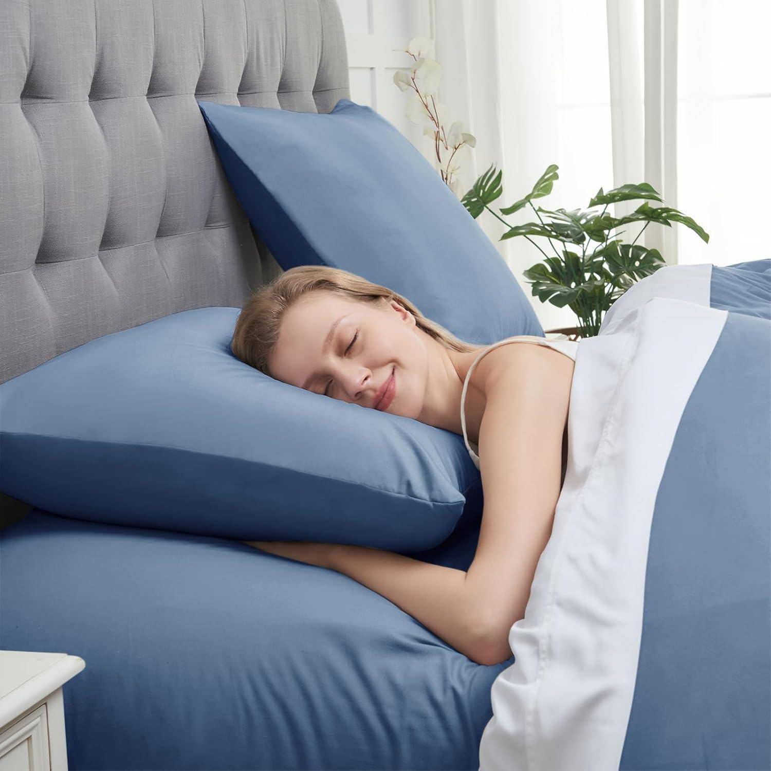 Eine Person, die friedlich auf einem Bett mit blauen Bettwäsche und Kissen schläft, in der Nähe einer Pflanze, was Entspannung und Komfort vermittelt.