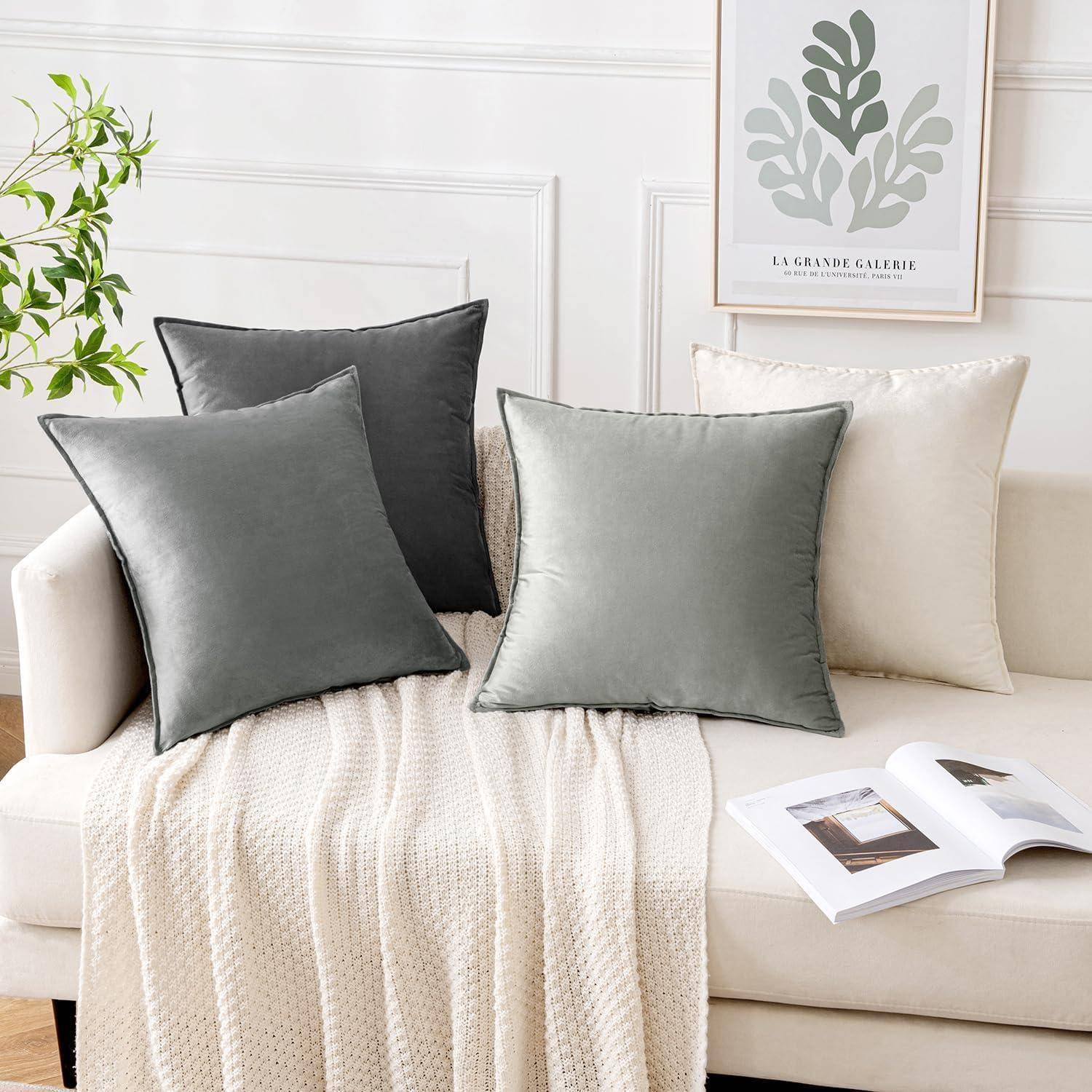 Sofa mit drei grauen Kissen und einer darüber geworfenen Decke, neben einem aufgeschlagenen Buch auf einem Holzcouchtisch, vor einem gerahmten botanischen Kunstdruck an der Wand.