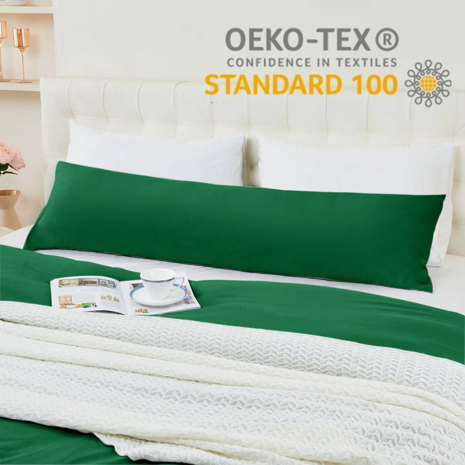 Ein grünes Körperkissen auf einem Bett mit weißer Bettwäsche in einem hellen Schlafzimmer. Darüber ist der Aufdruck „OEKO-TEX Vertrauen in Textilien, Standard 100