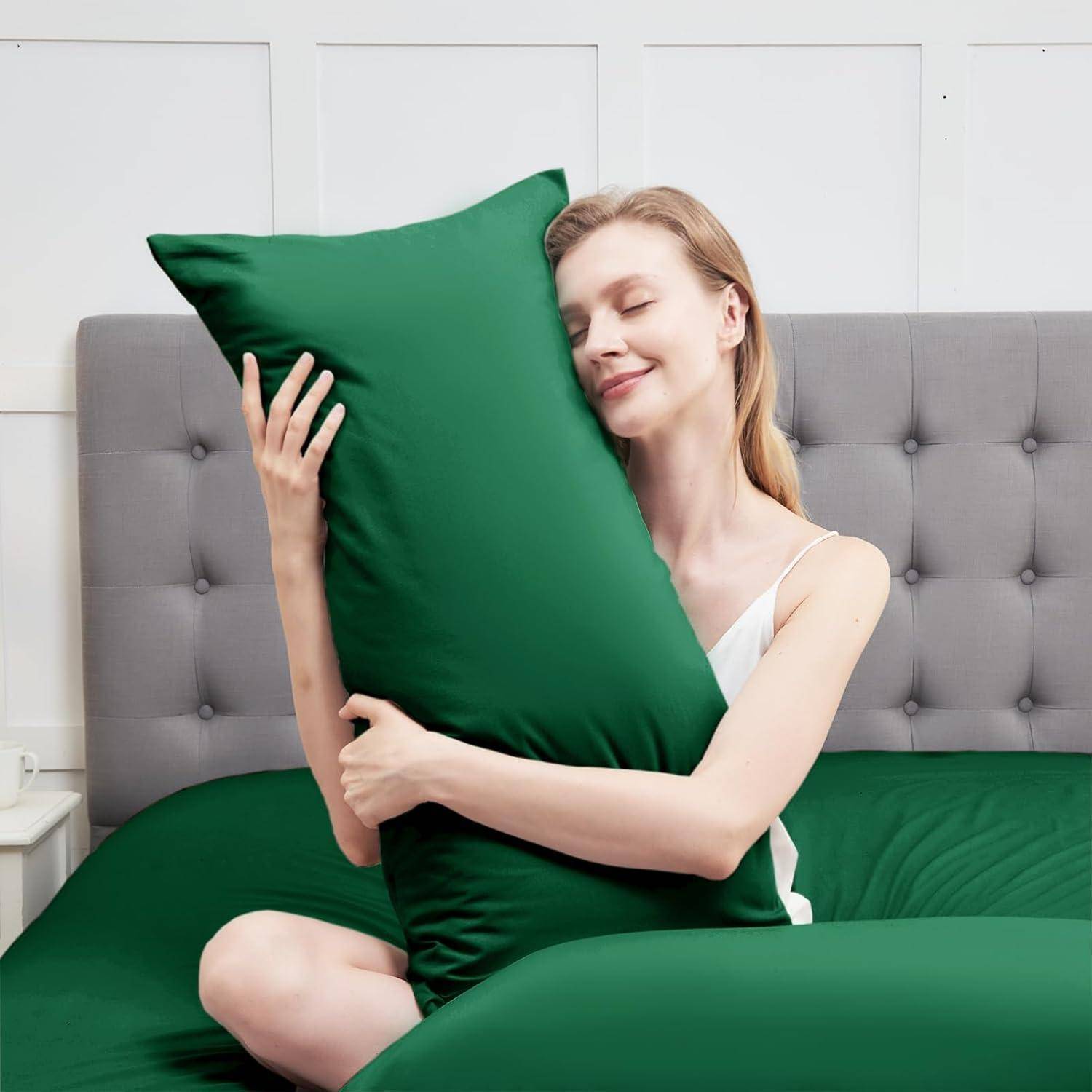 Eine lächelnde Person umarmt ein großes grünes Kissen in einem gemütlichen, minimalistischen Schlafzimmer.