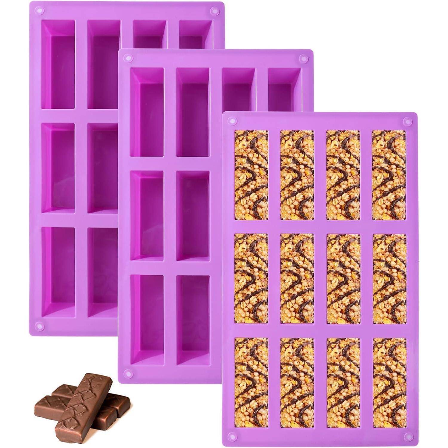 Drei rosa Silikonformen zum Herstellen von Schokoladentafeln, mit sichtbaren Fächern. Einige fertige Schokoladentafeln liegen in der Nähe.