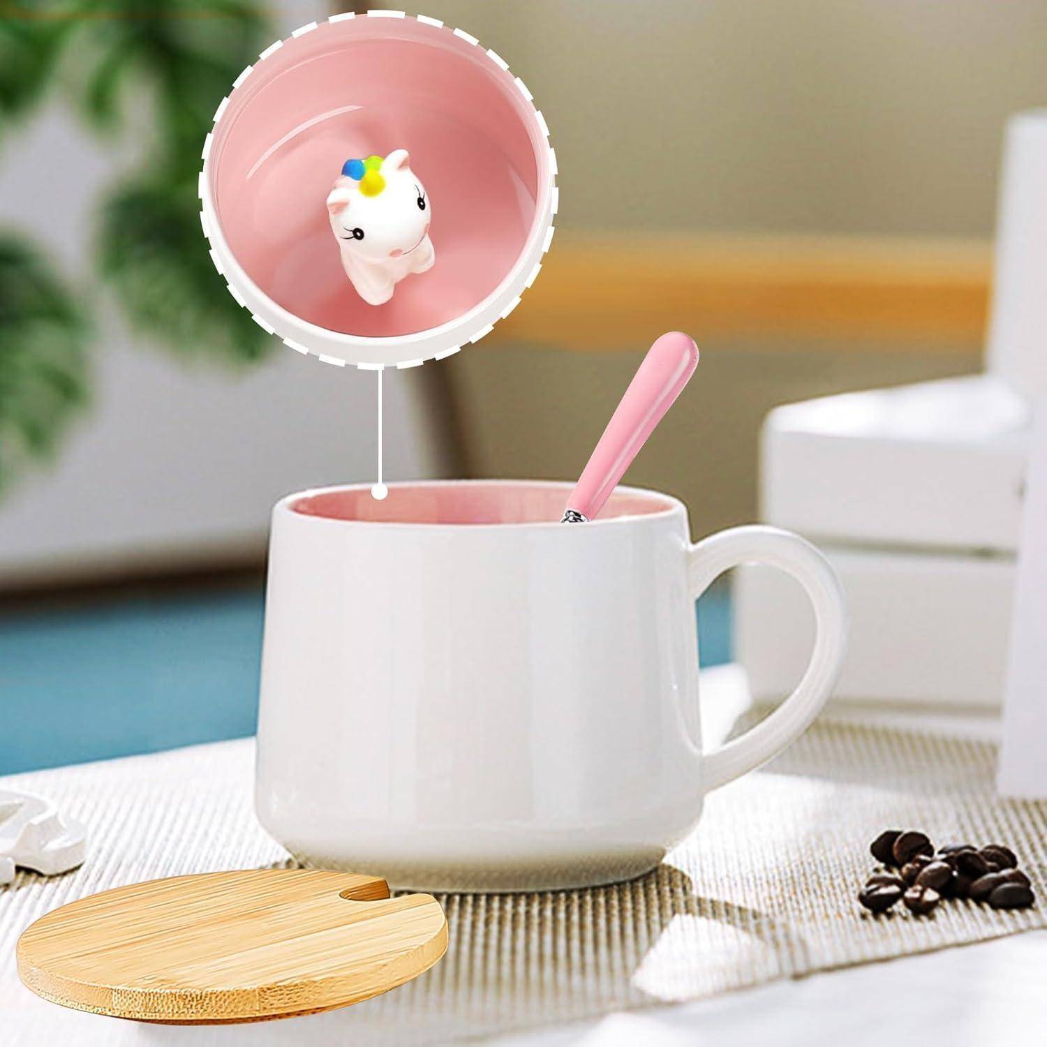 Eine weiße Tasse mit rosafarbener Innenseite und einer Einhornfigur am Boden, neben einem Holzdeckel und Kaffeebohnen.