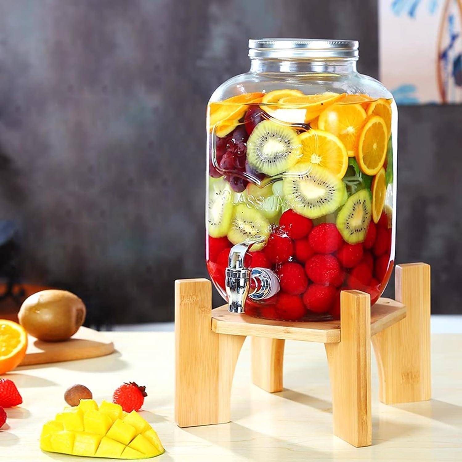 Ein Glaskrug, gefüllt mit geschnittenen Früchten wie Orangen, Kiwis und Beeren, steht auf einem Holzständer und deutet auf ein erfrischendes, fruchtiges Getränk hin.