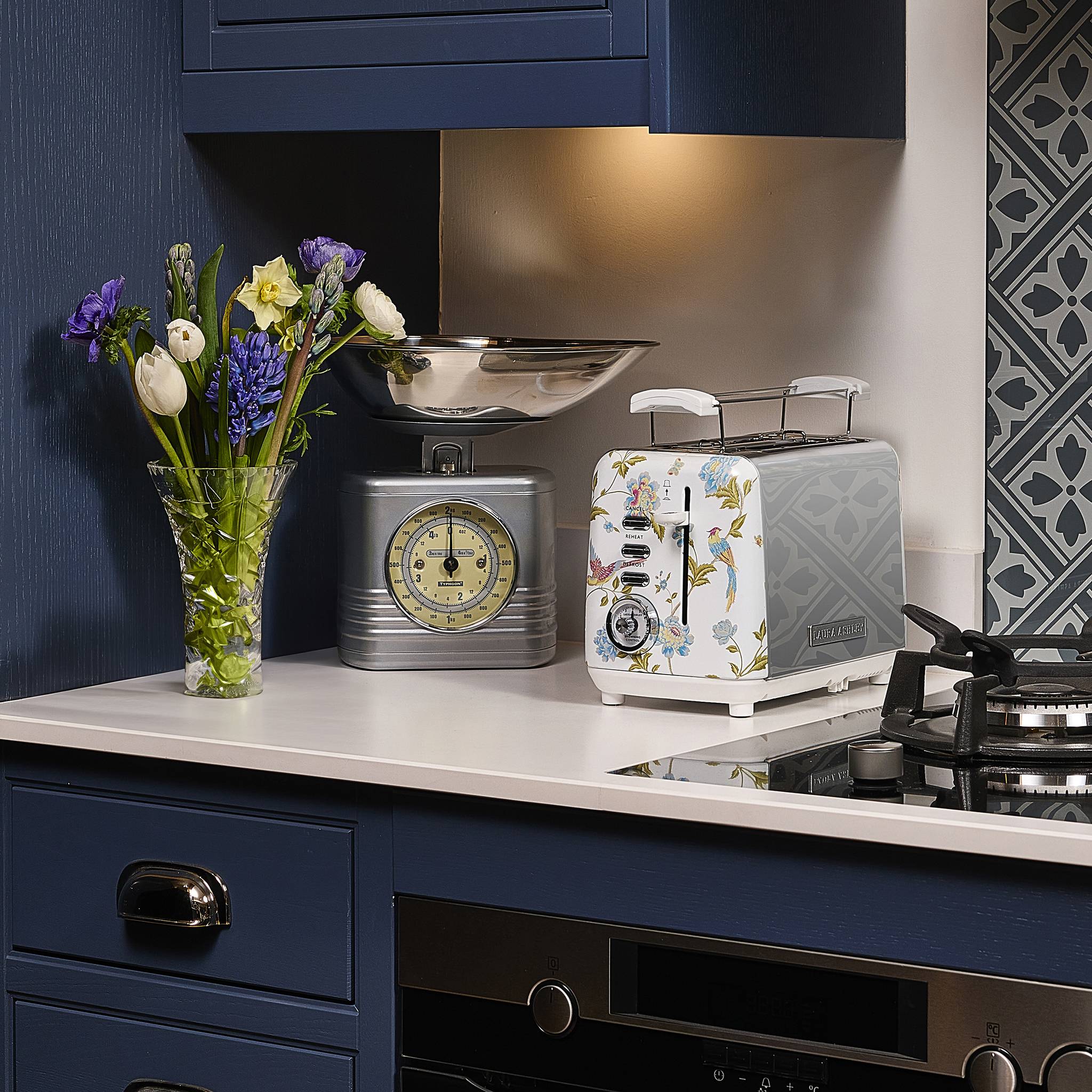 Eine Küchenarbeitsplatte mit einer Blumenvase, einer Vintage-Waage mit einer Schüssel und einem dekorativen Toaster in einer blaugeprägten Küche.