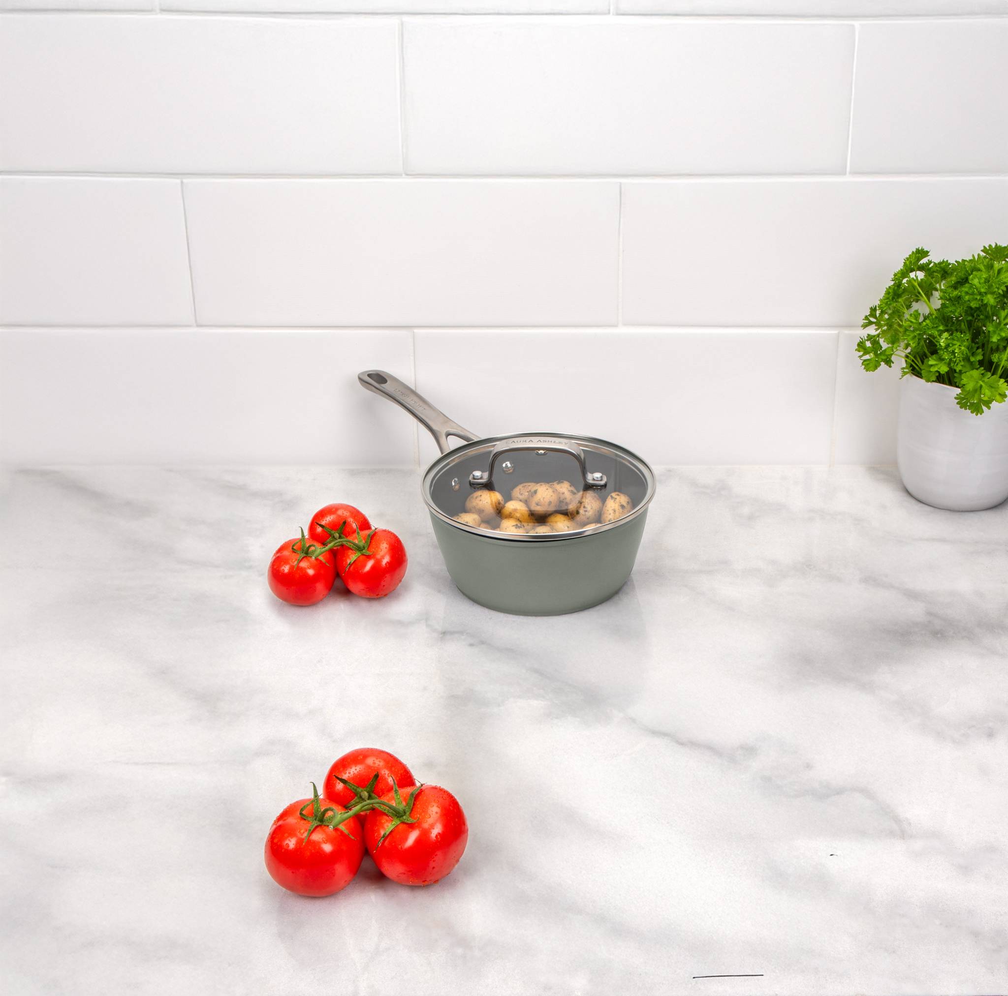 Eine Pfanne mit Pilzen und Tomaten auf einer Marmorarbeitsplatte vor einer weiß gefliesten Wand.