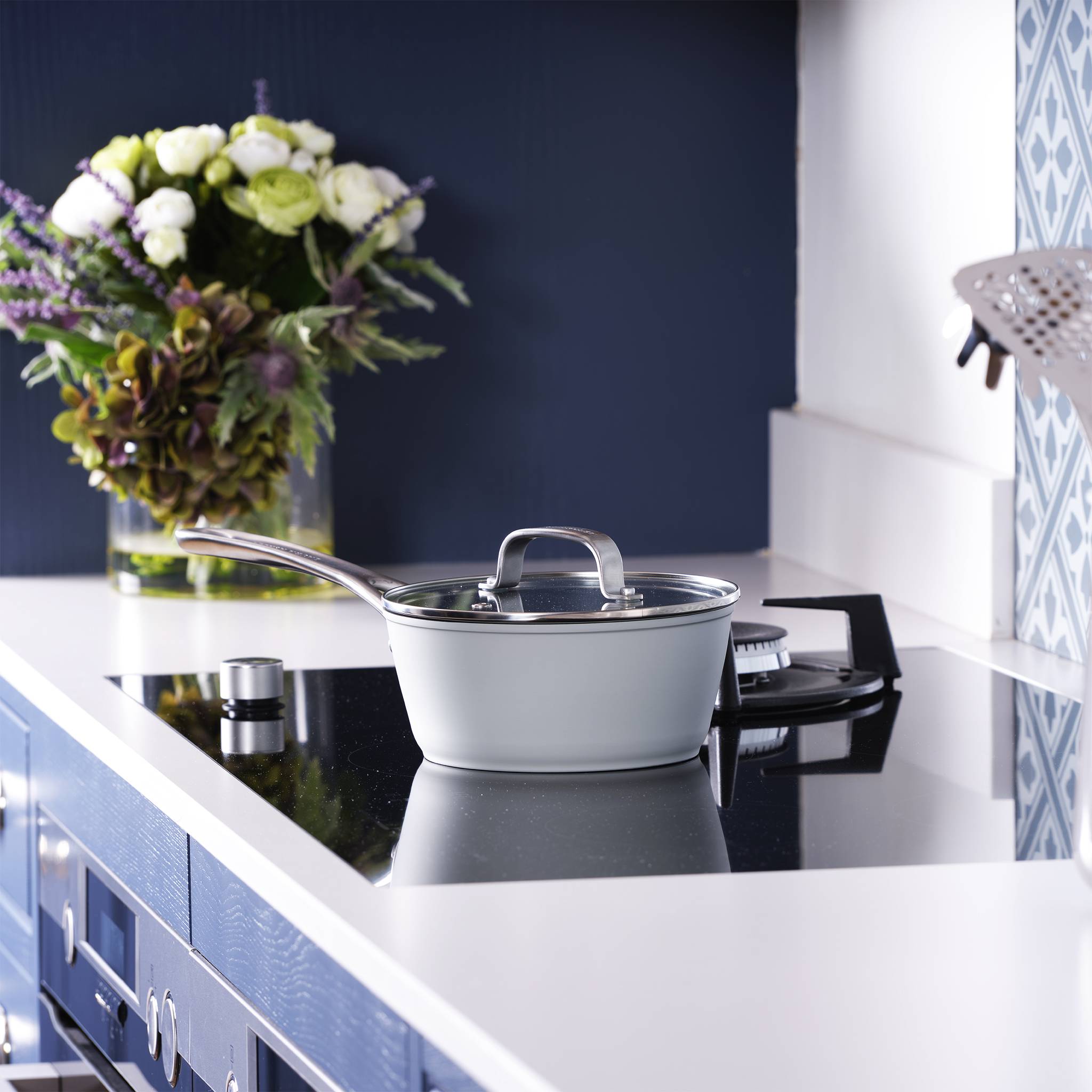 Ein Topf mit Deckel steht auf einer Kochplatte in einer modernen Küche. Im Hintergrund befindet sich eine Vase mit einem Blumenstrauß.